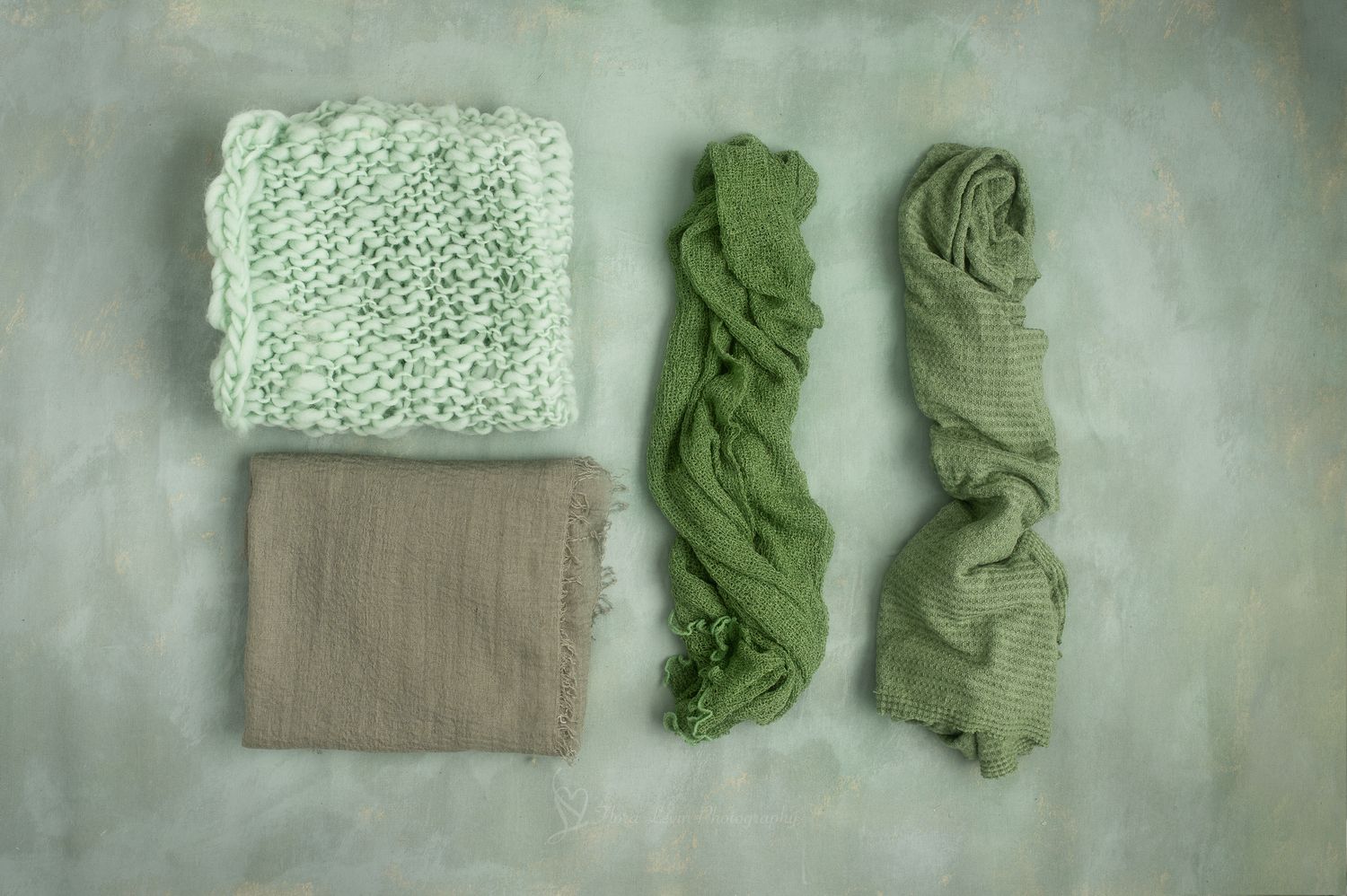 Green tones knit wraps and blankets arranged flat on a textured green background for newborn photography.