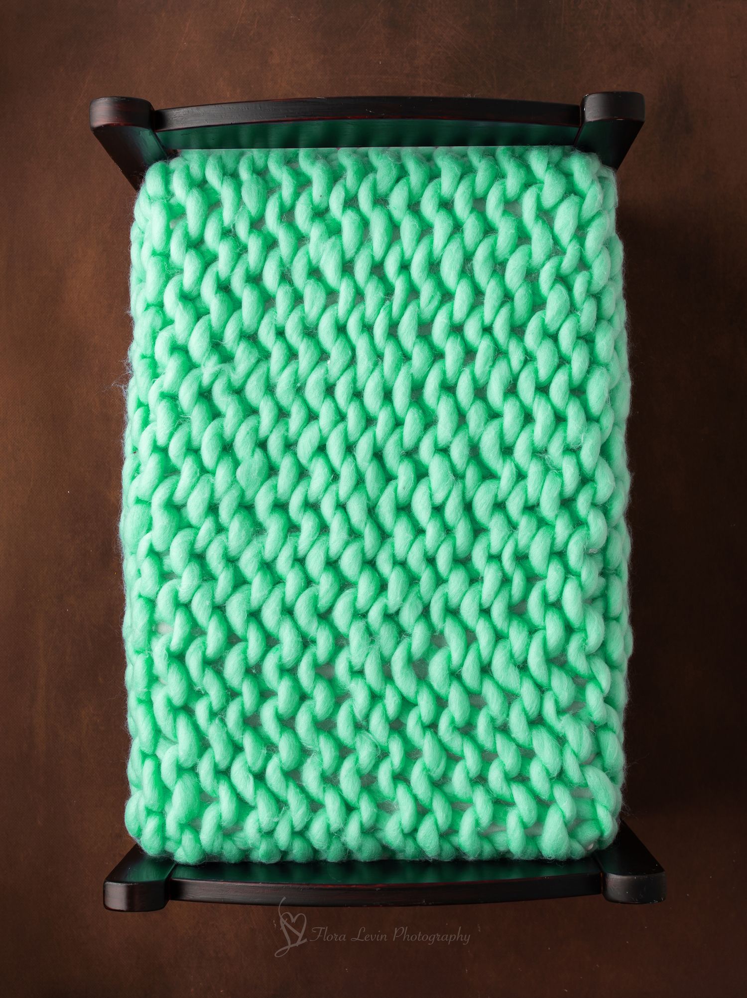 Small dark wood bench with a chunky knit mint green blanket, perfect for newborn photography props.