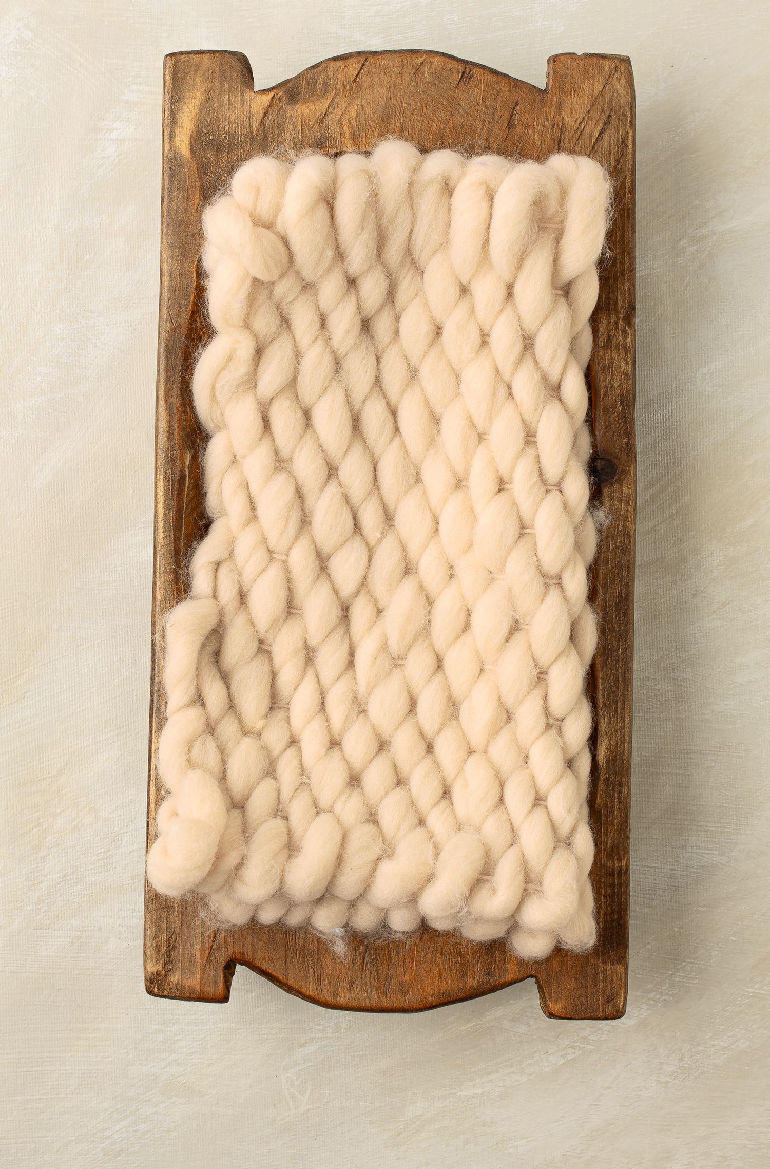 Chunky cream wool yarn wrapped around a rustic wooden hand carder on a neutral background.