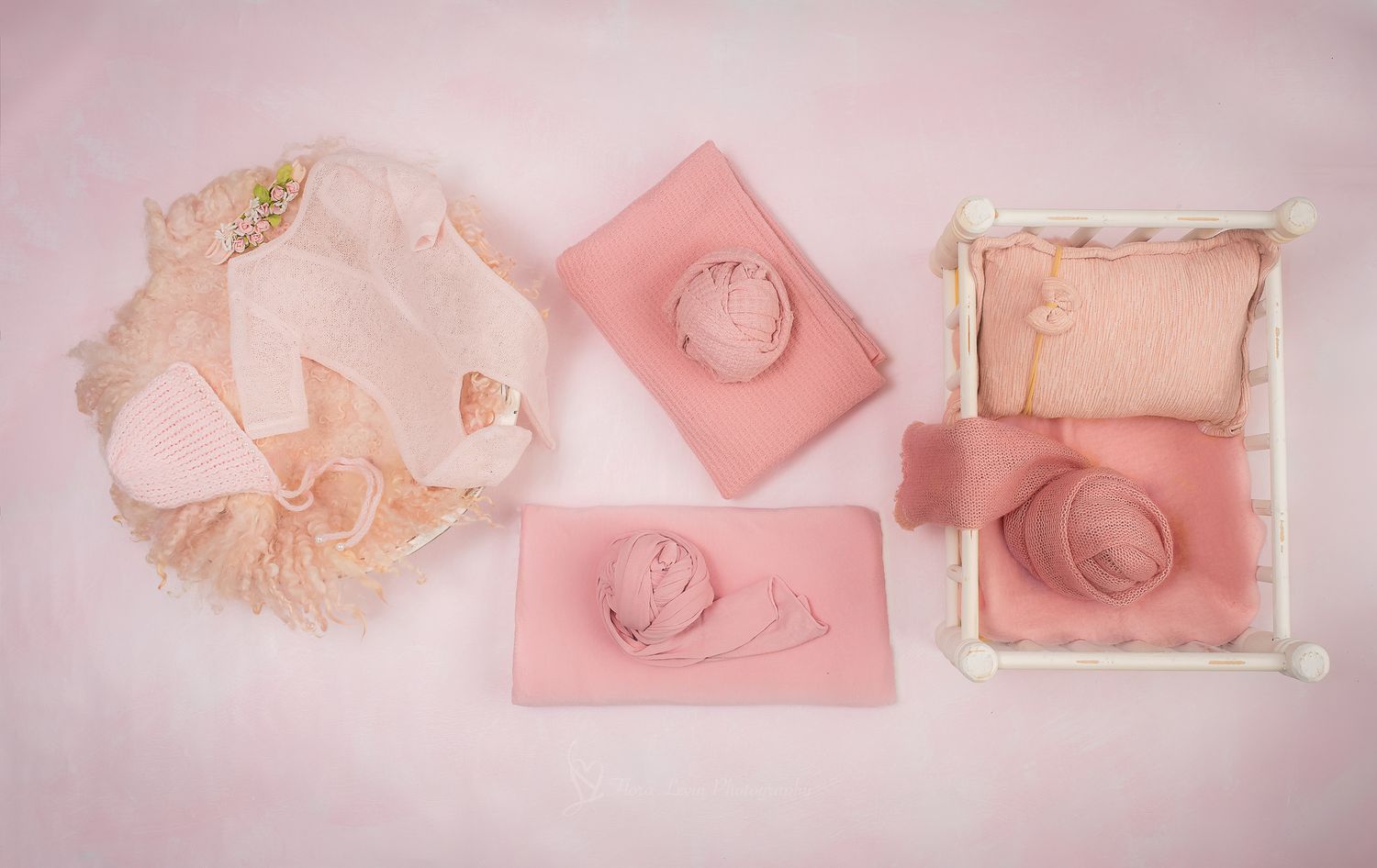 Pink newborn photography props set including lace bonnet, wraps, and a mini wooden bed on a soft pink background.