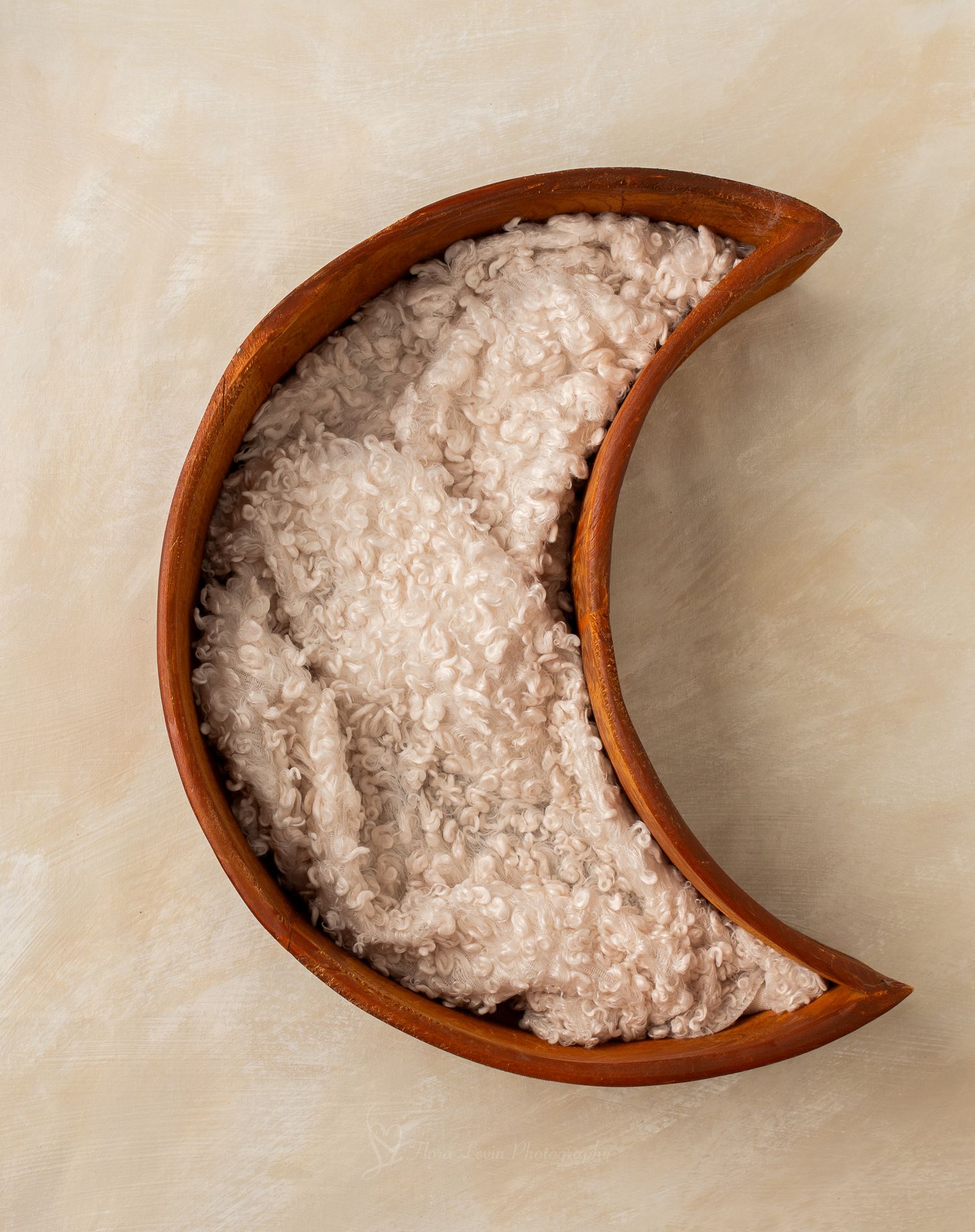 Crescent moon-shaped wooden bowl filled with soft, fluffy cream-colored faux fur fabric on a neutral background.