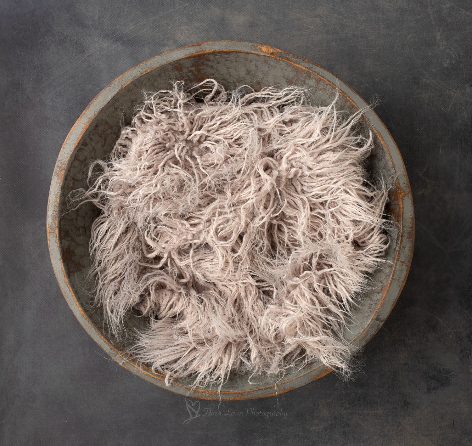 Fluffy cream curly fur filler in a gray rustic wooden bowl on gray background for newborn photography prop.