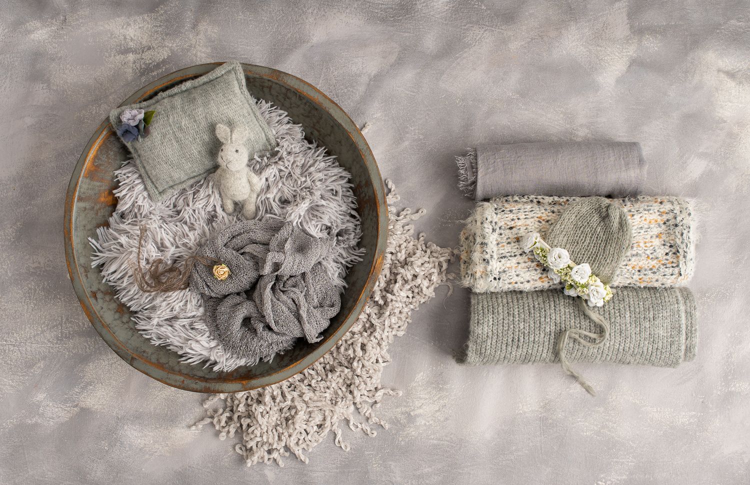 Newborn photography props including a gray wooden bowl with gray props and different shades of gray wraps.