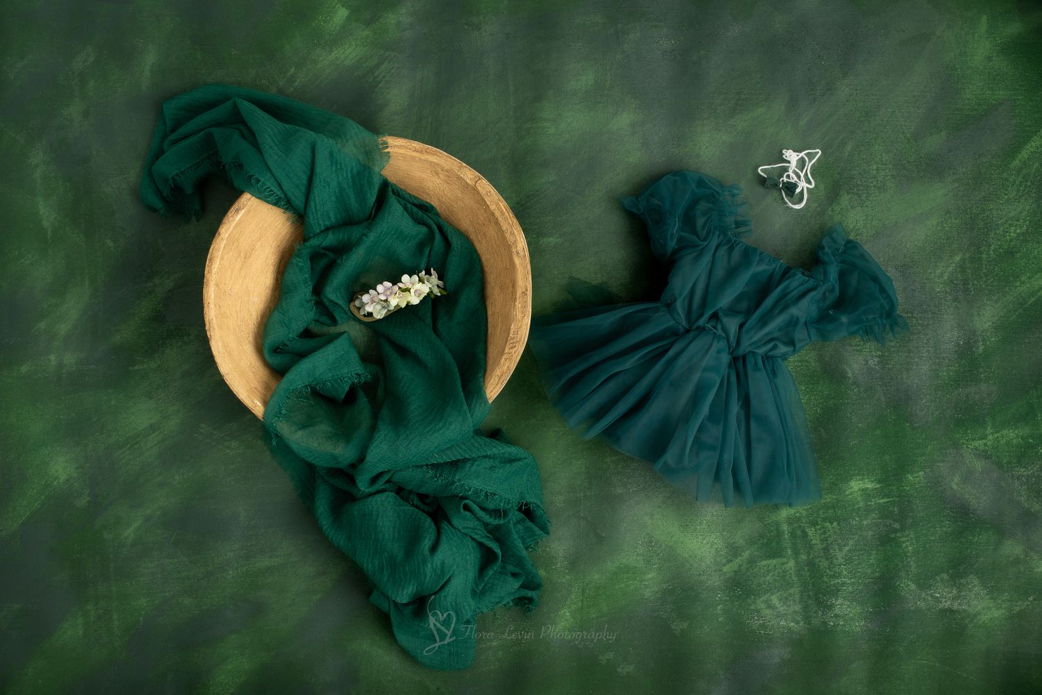 Emerald green chiffon fabric draped in wooden bowl with tiny white flowers and matching ruffled dress on green backdrop.