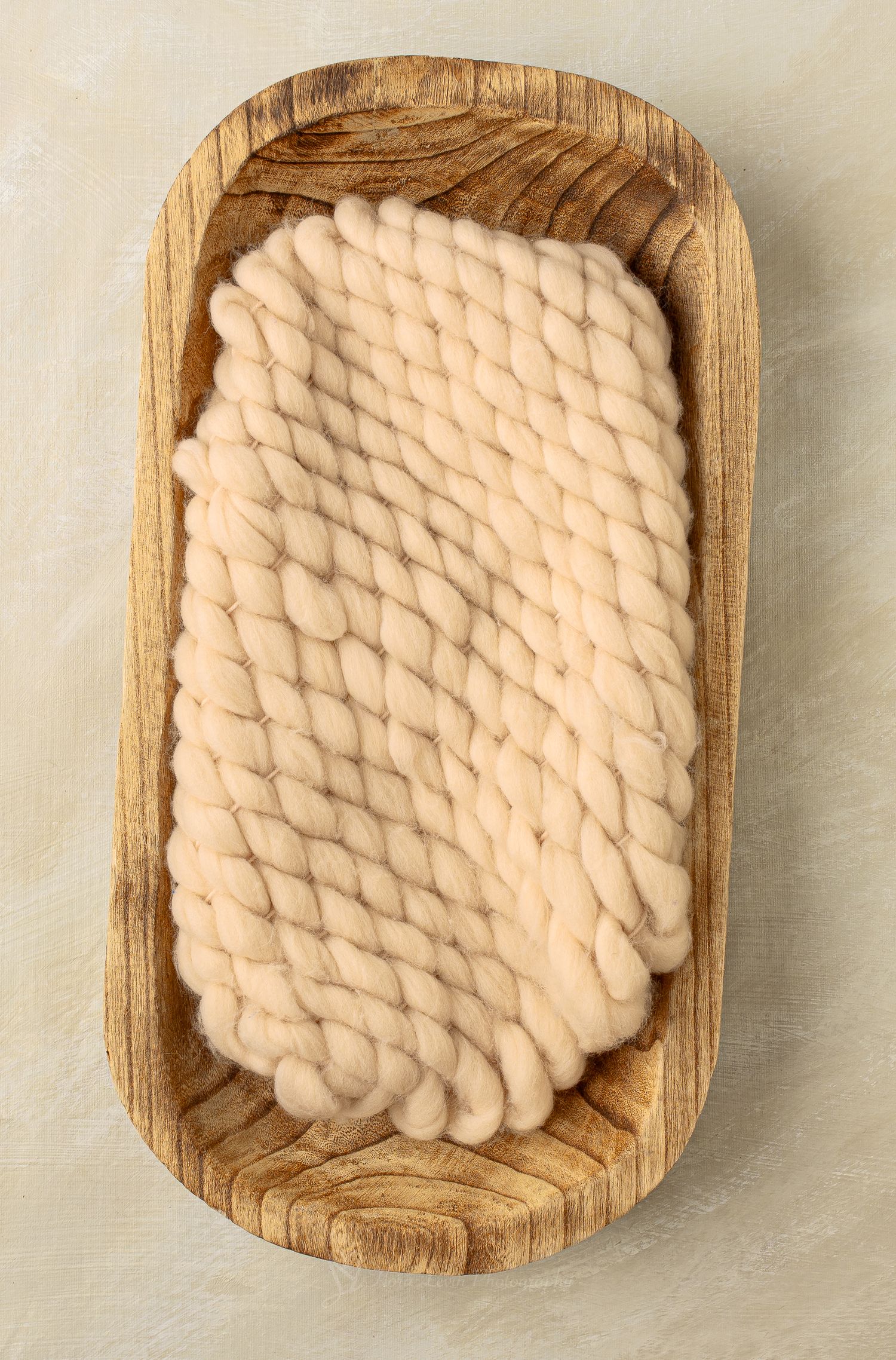 Chunky cream wool roving displayed in a rustic oval wooden tray on a neutral background.