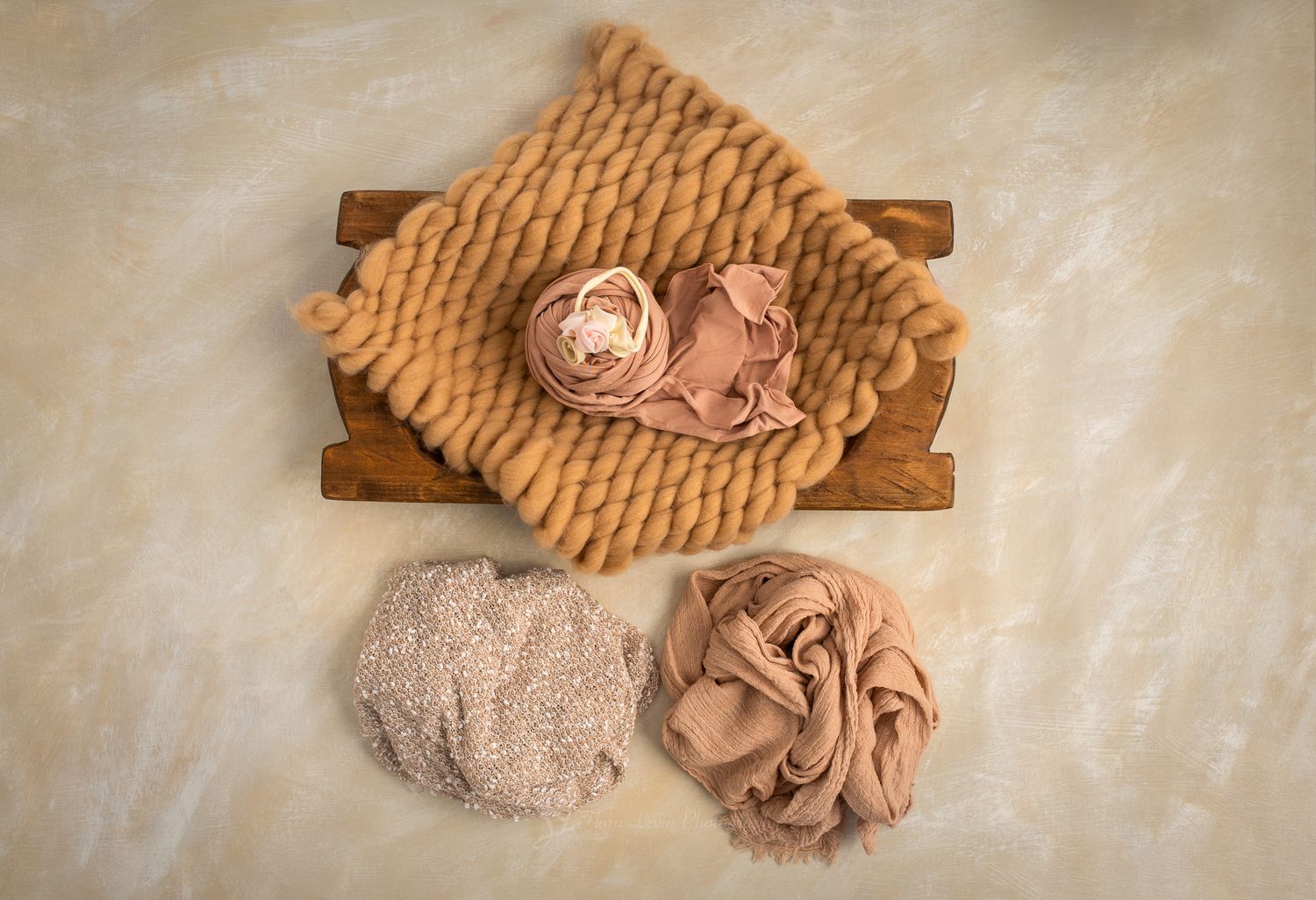 Newborn photography props featuring a wooden crate, tan knit blanket, and three rolled fabric wraps in neutral tones.