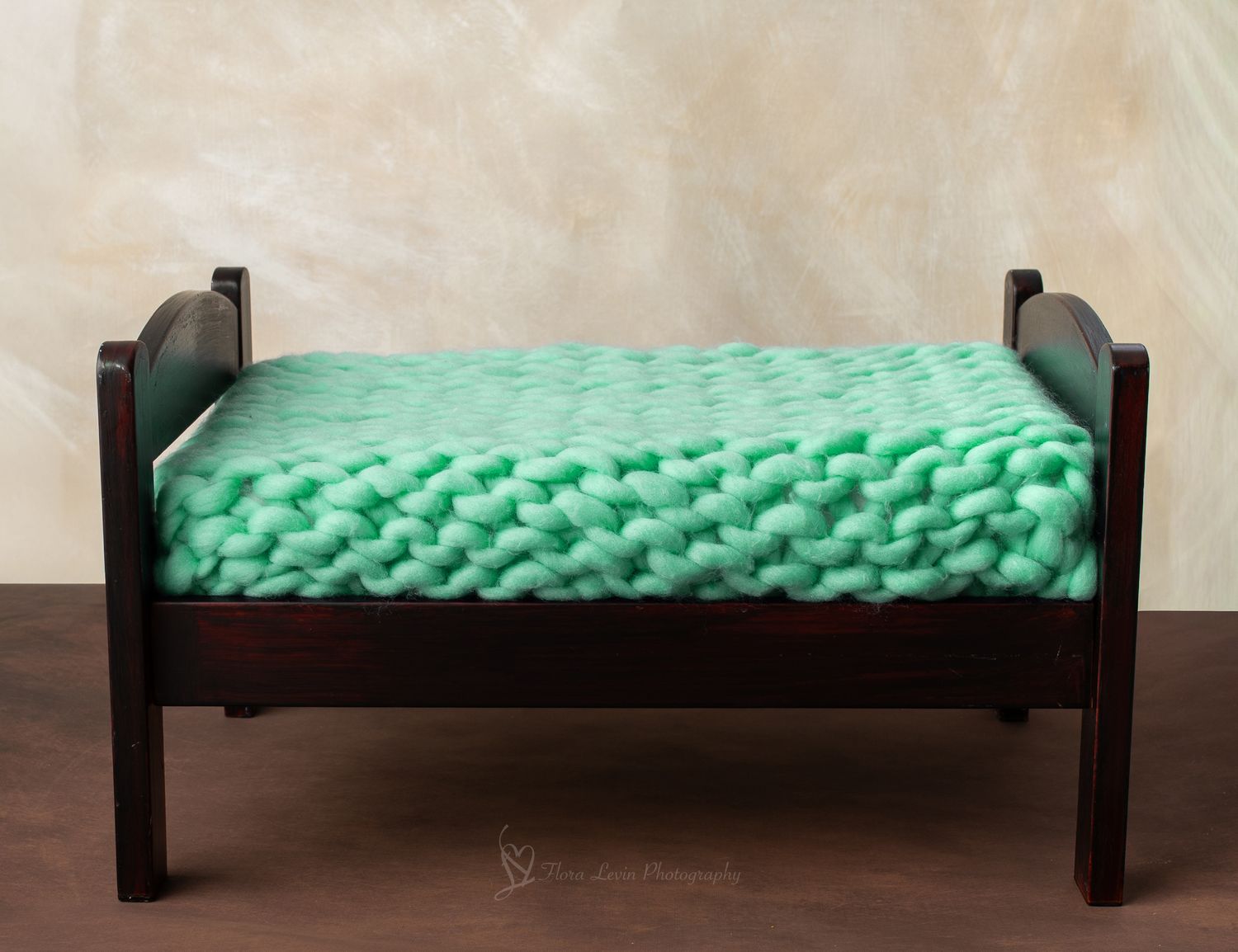 Small dark wood bench with a chunky knit mint green blanket, perfect for newborn photography props.