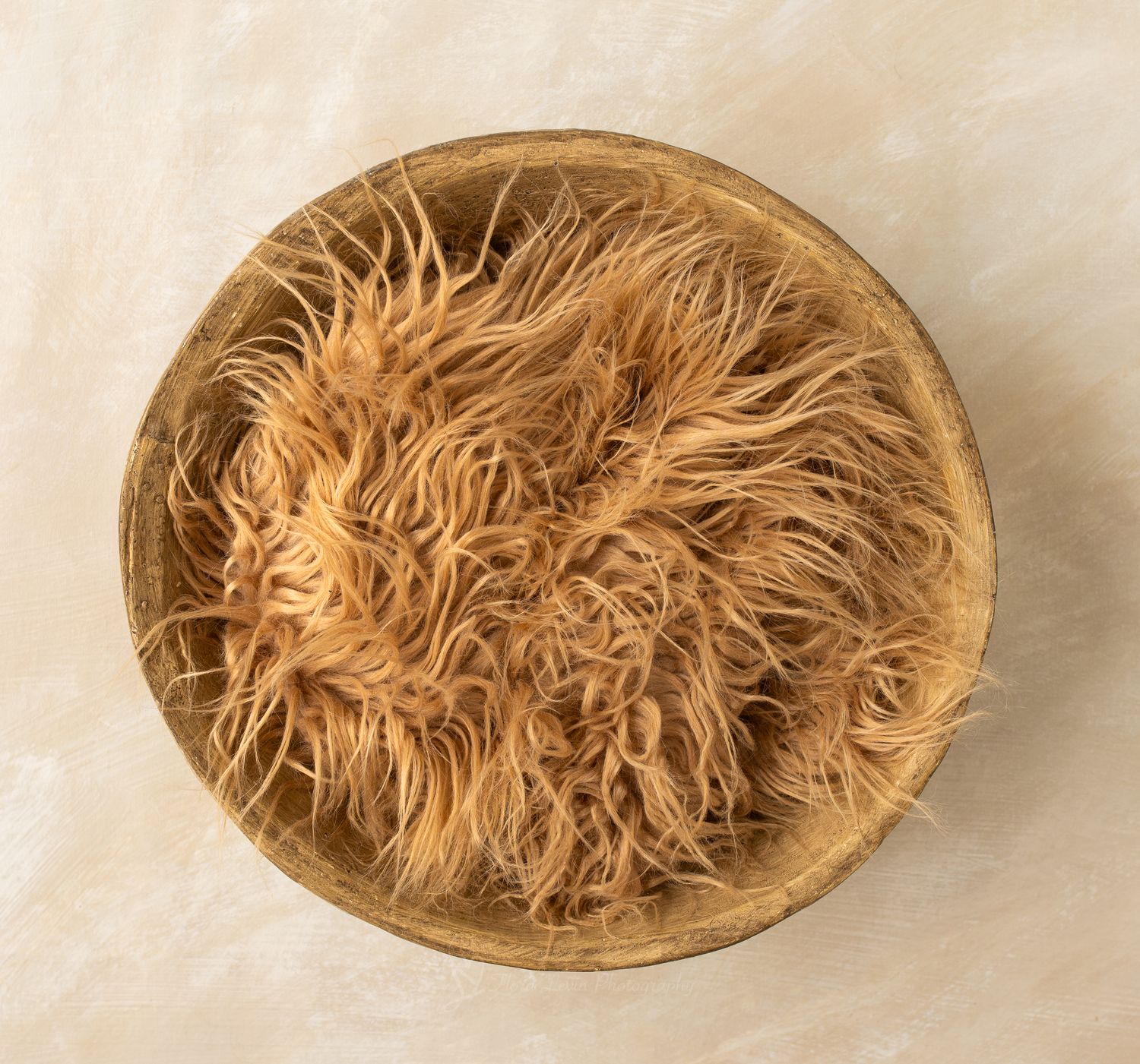 Fluffy caramel-colored faux fur nestled inside a round wooden bowl, perfect for newborn photography props.