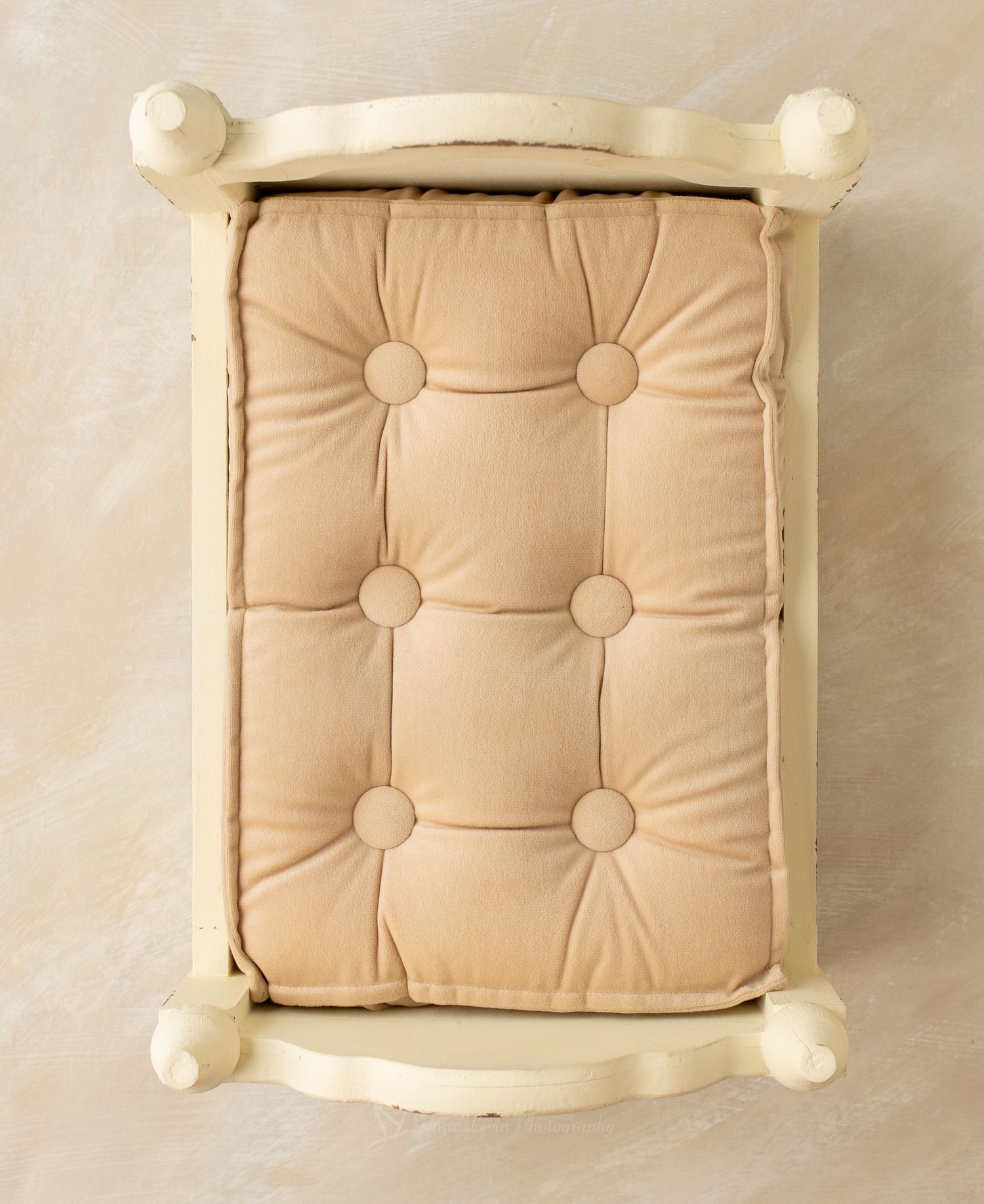 Cream wooden bed with tufted beige cushion mattress, perfect for newborn photography