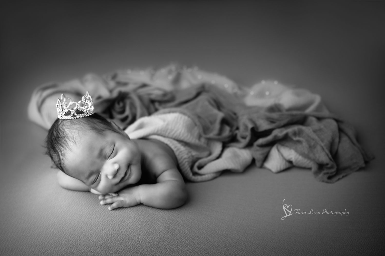 Black and white portrait of a smiling sleeping newborn baby girl wrapped in soft fabric with a delicate crown accessory. Black &white photo.