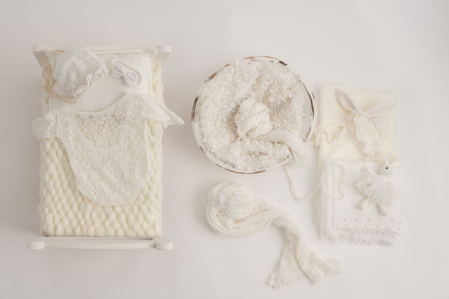 White and ivory cream newborn photography props set including a mini bed, basket, bonnet, wrap, and stuffed animal on white background.