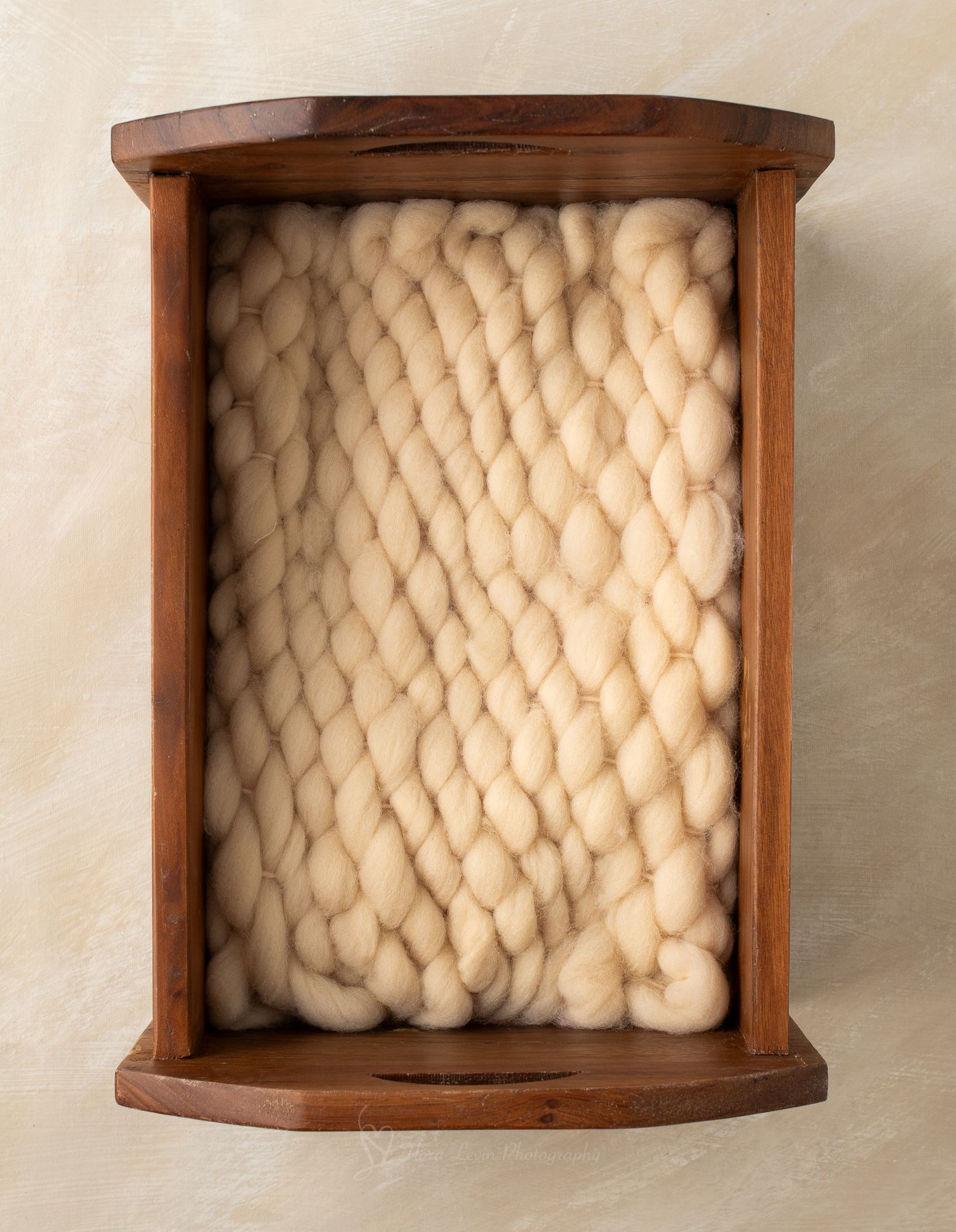 Chunky cream wool yarn displayed in a curved walnut wood bed photographed from above.