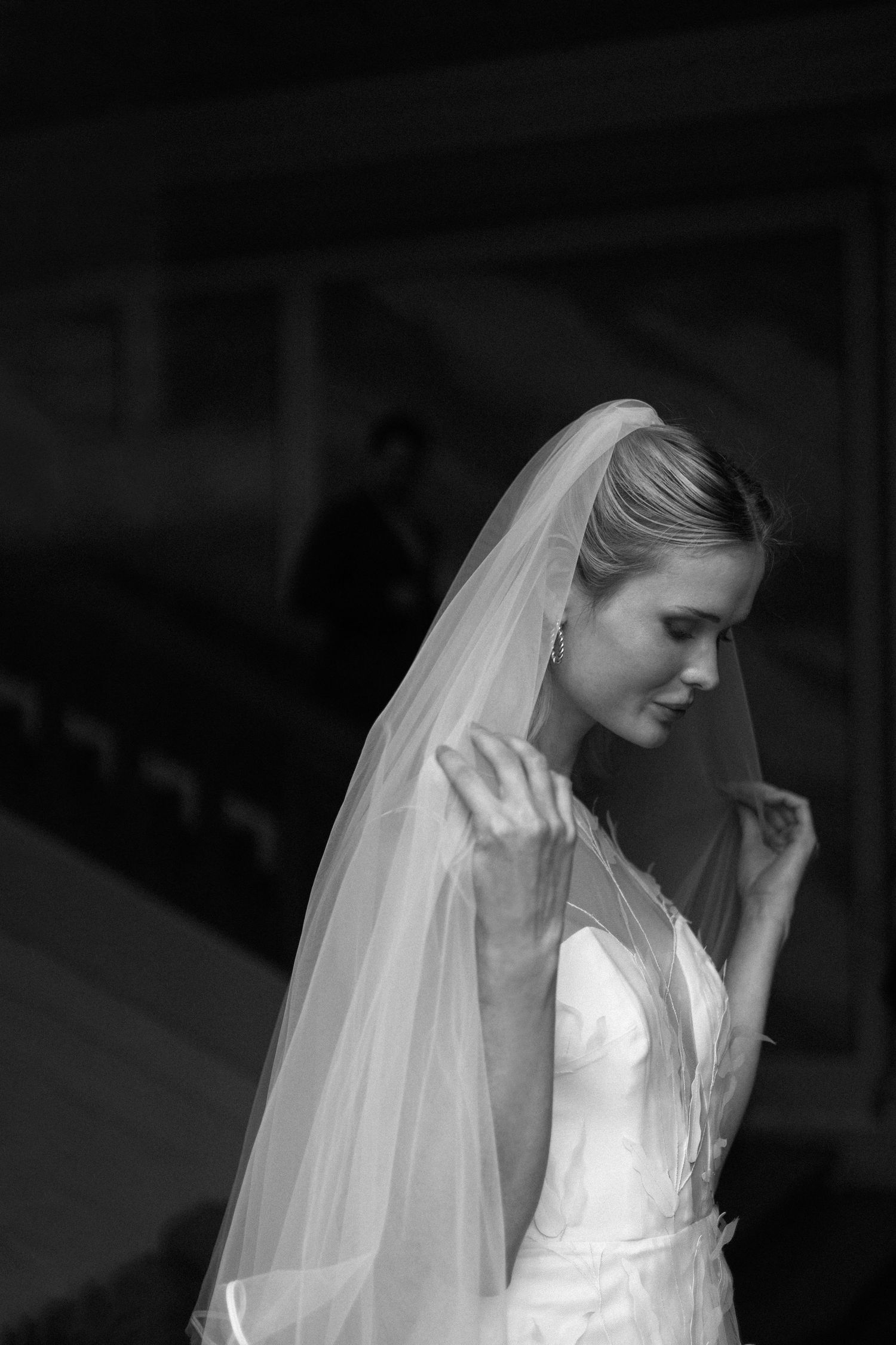 A bride wearing a white wedding dress and long flowing veil is captured in a black and white portrait series.