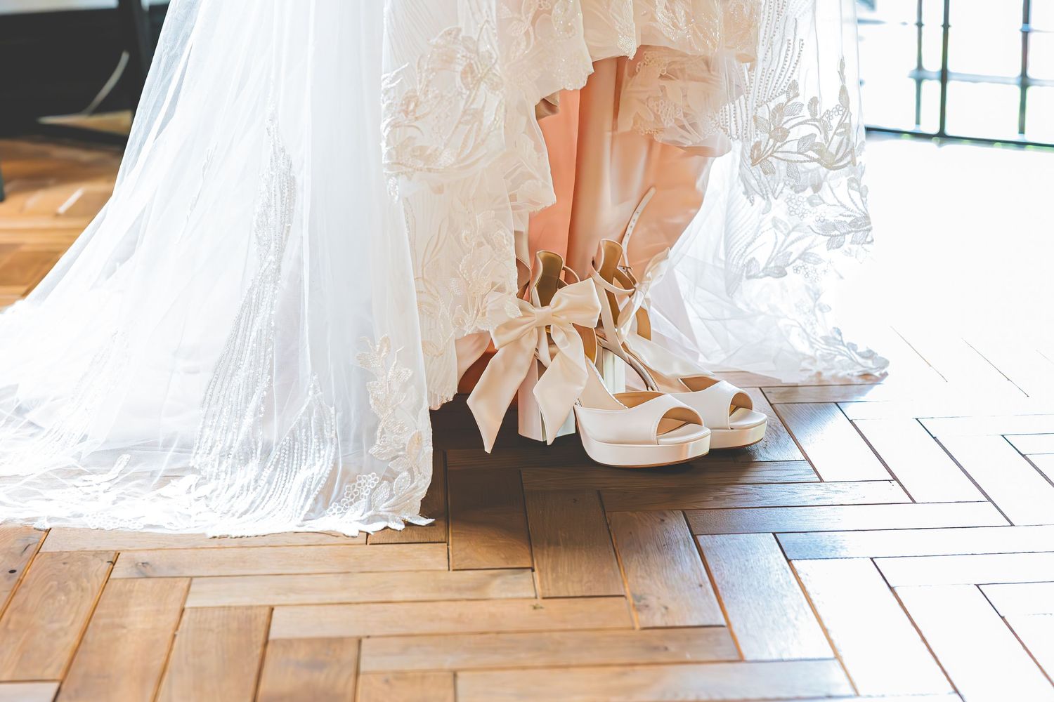 Detail shot showing elegant white wedding dress spreading across rustic hardwood flooring with natural light.