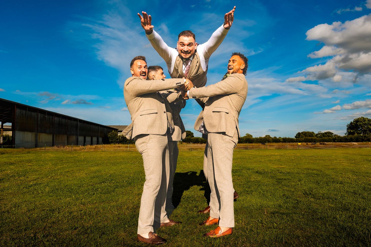 Groom gets thrown into the air by groomsmen in a green field