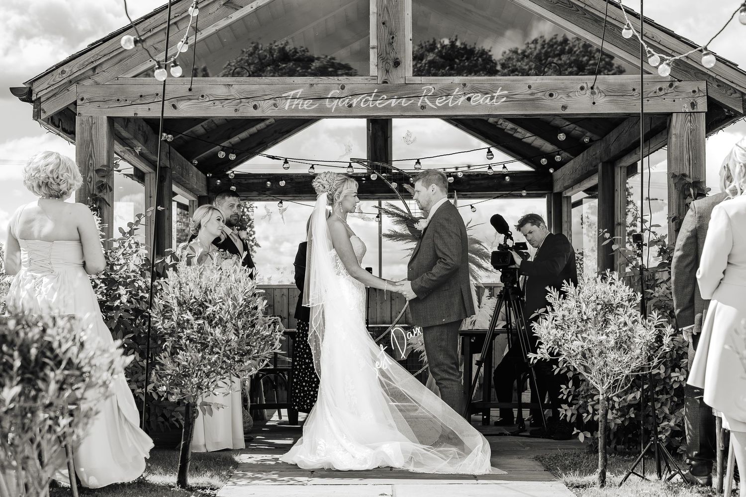 A black and white panoramic collage showing multiple scenes from an outdoor wedding ceremony and reception.