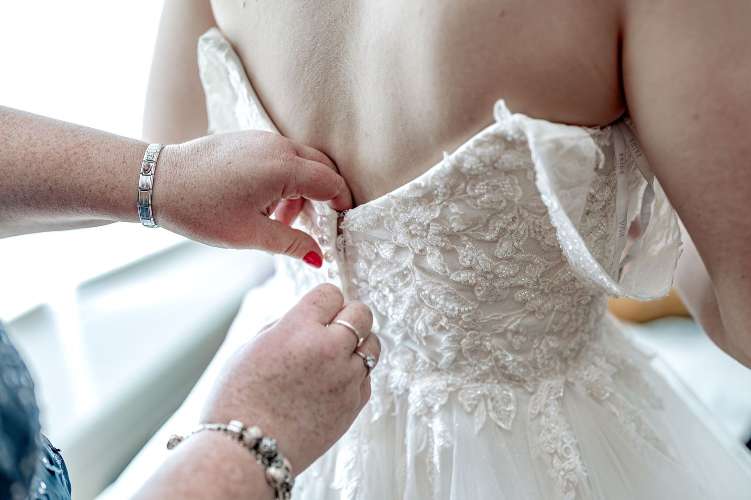 Close-up shots of adjusting and fastening a white lace wedding dress with delicate details and buttons throughout.