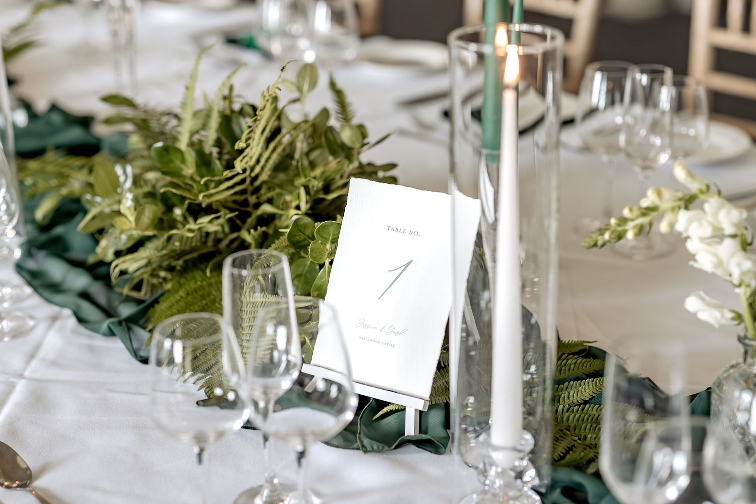 Elegant wedding table setting with white linens, tall candles, green eucalyptus garland and crystal glassware.