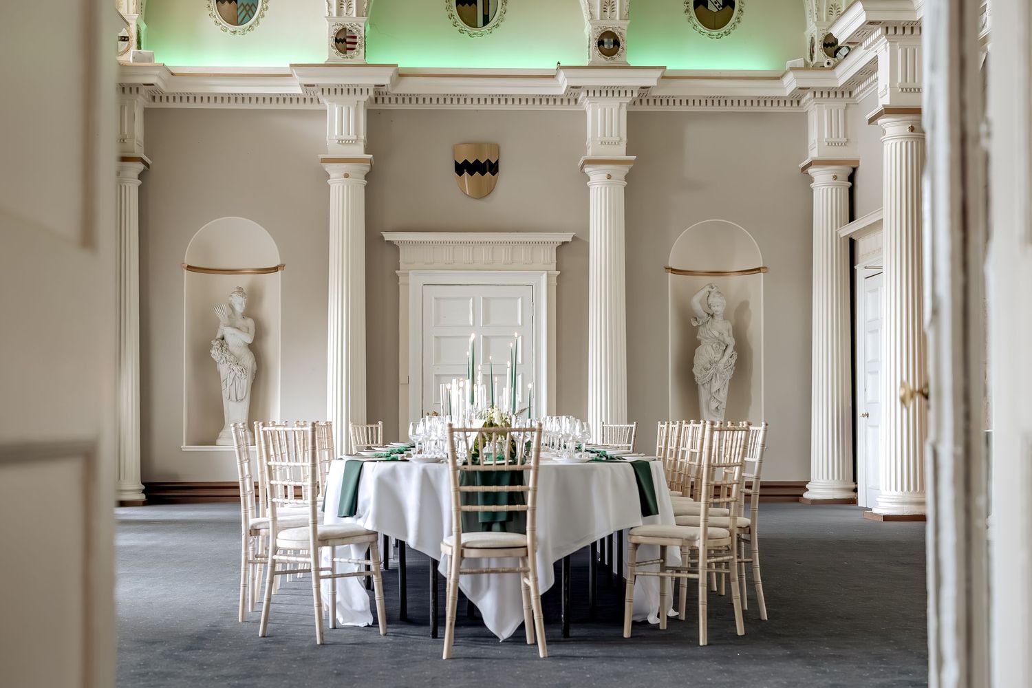 Elegant white banquet hall with classic columns and round tables set for formal dining in a bright, airy space.