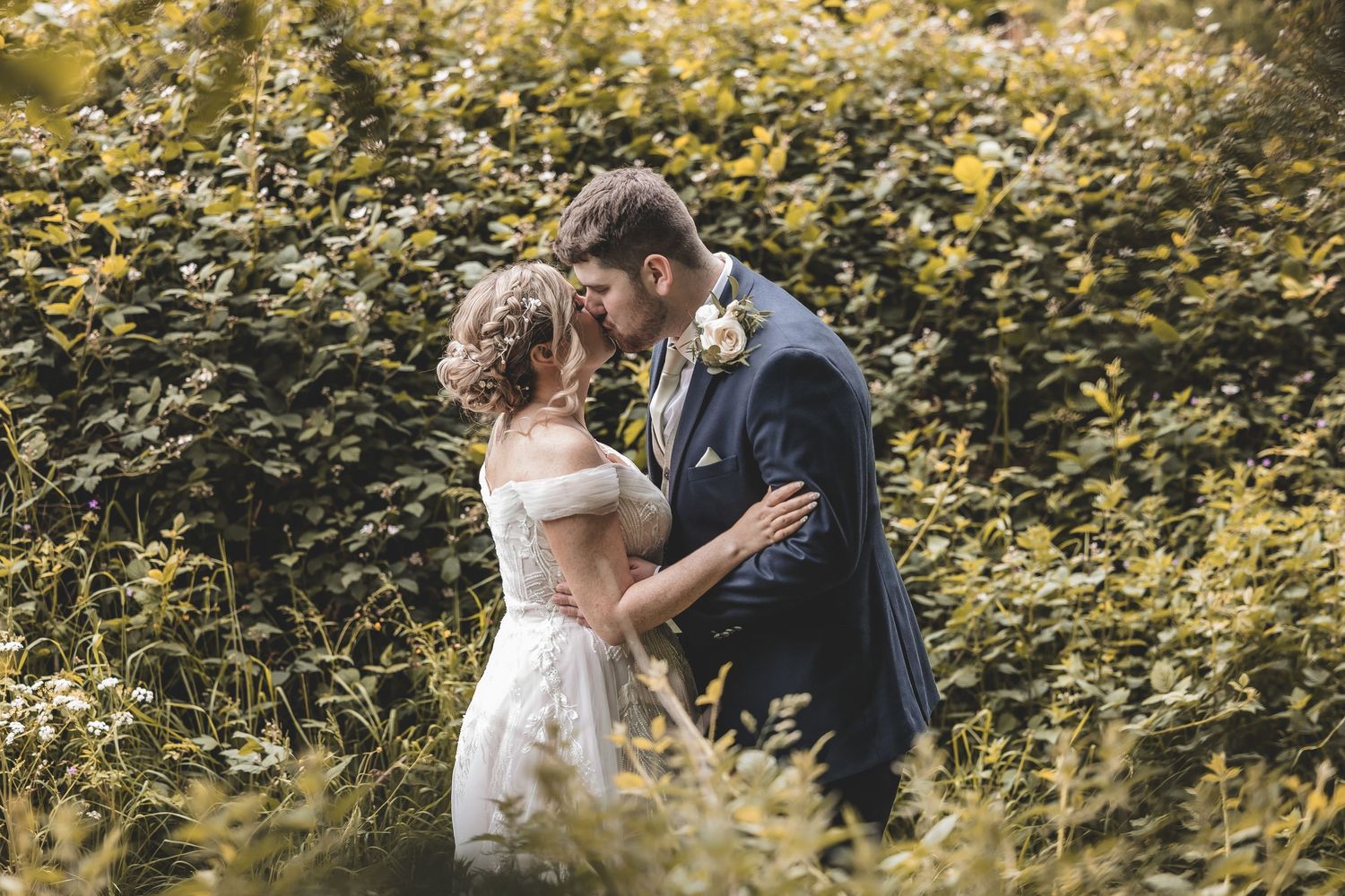 Unobtrusive Documentary wedding photo of a bride and groom sharing a kiss amongst the venues woodlands.