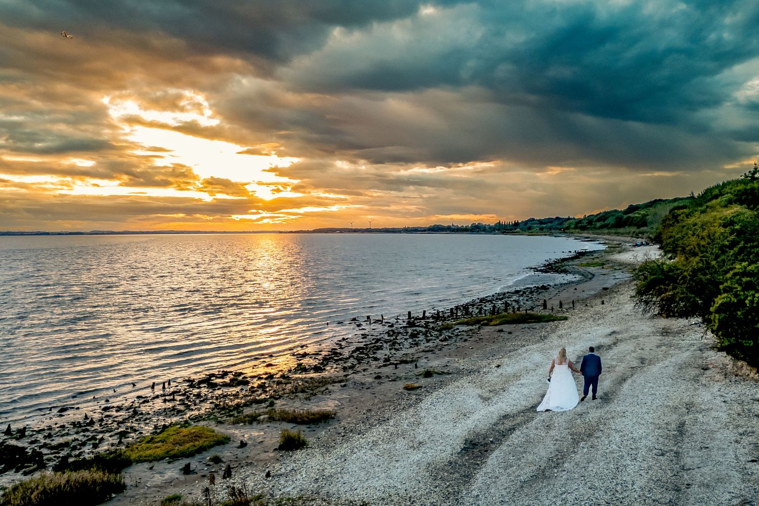 Dramatic coastal sunset panorama with rocky beach and dramatic clouds over the ocean. with a newly wed couple strolling along.
