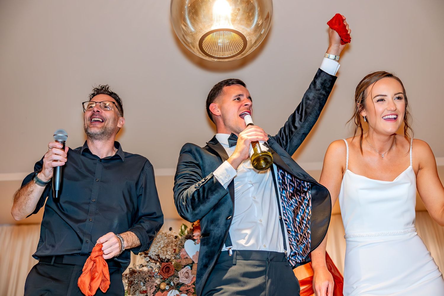 Bride and Groom celebrating with their wedding singer whilst standing on a table.