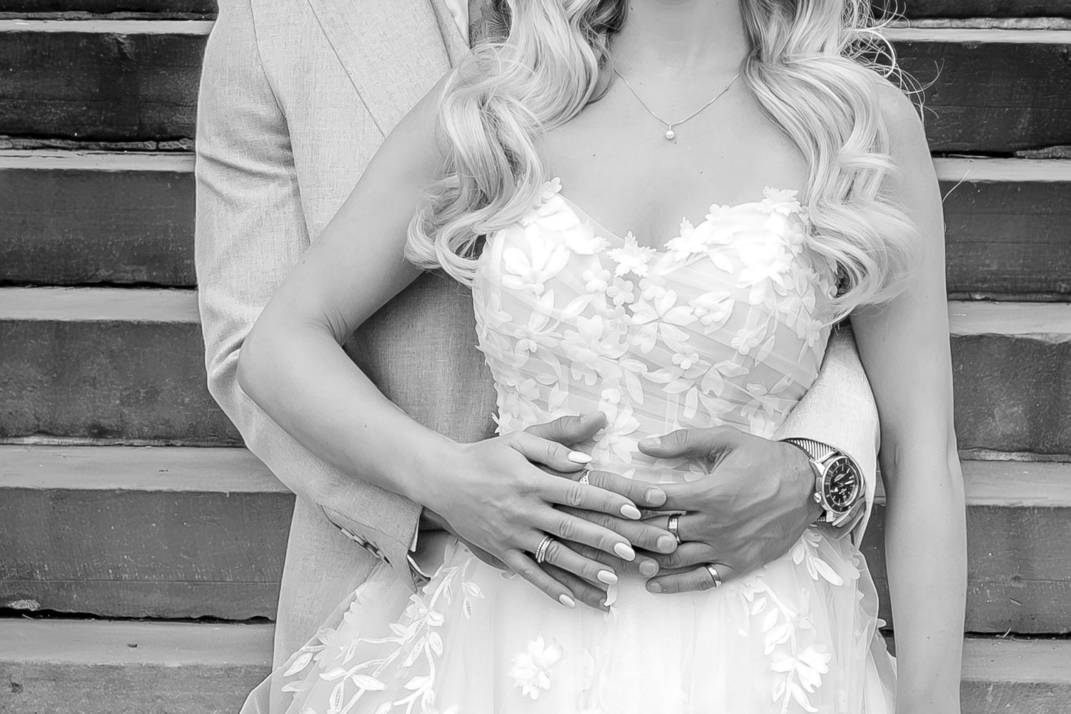 Black and white romantic wedding photo showing couple embracing on stairs with bride wearing lace strapless gown.