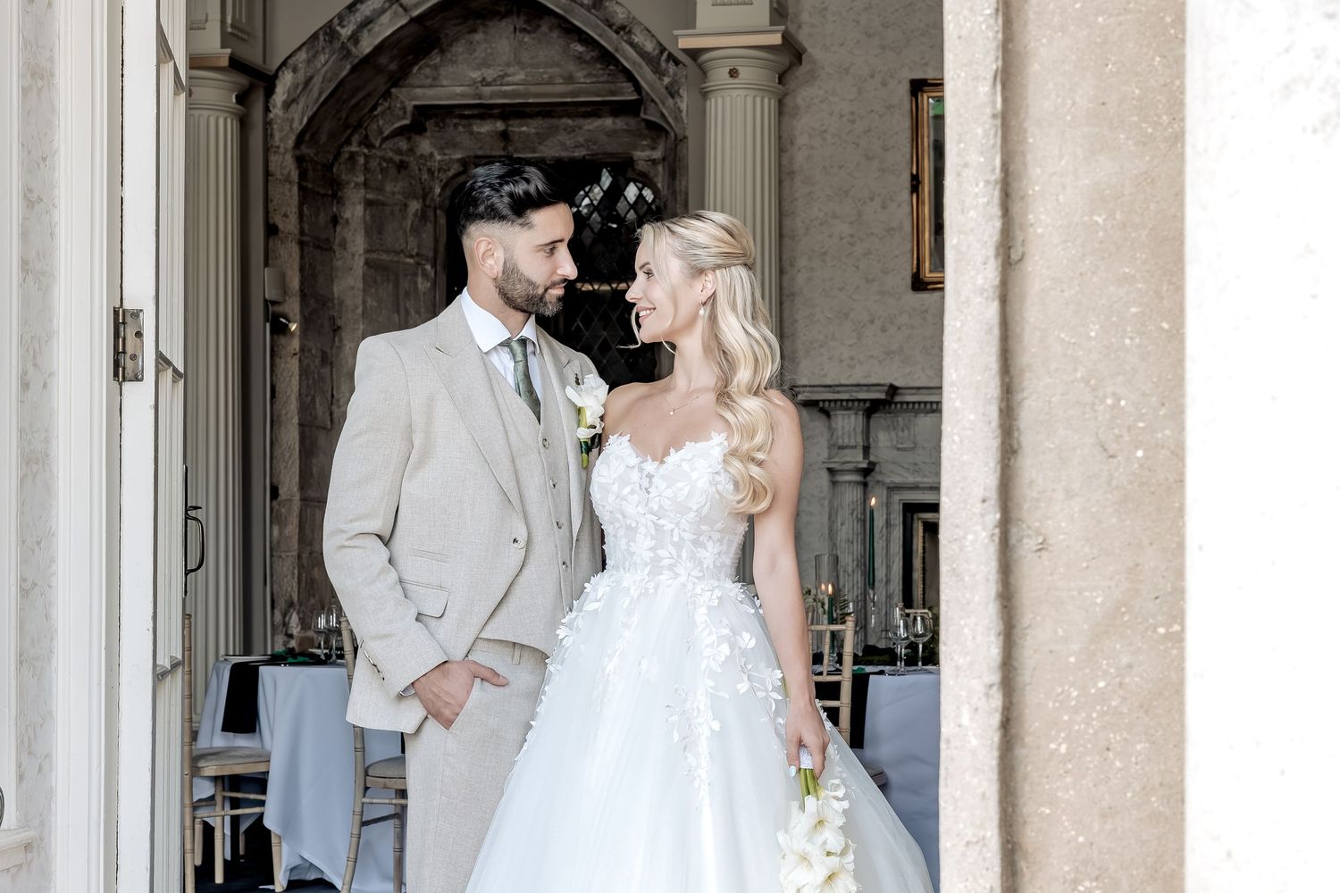 A couple in wedding attire poses together under a stone archway at an elegant venue.