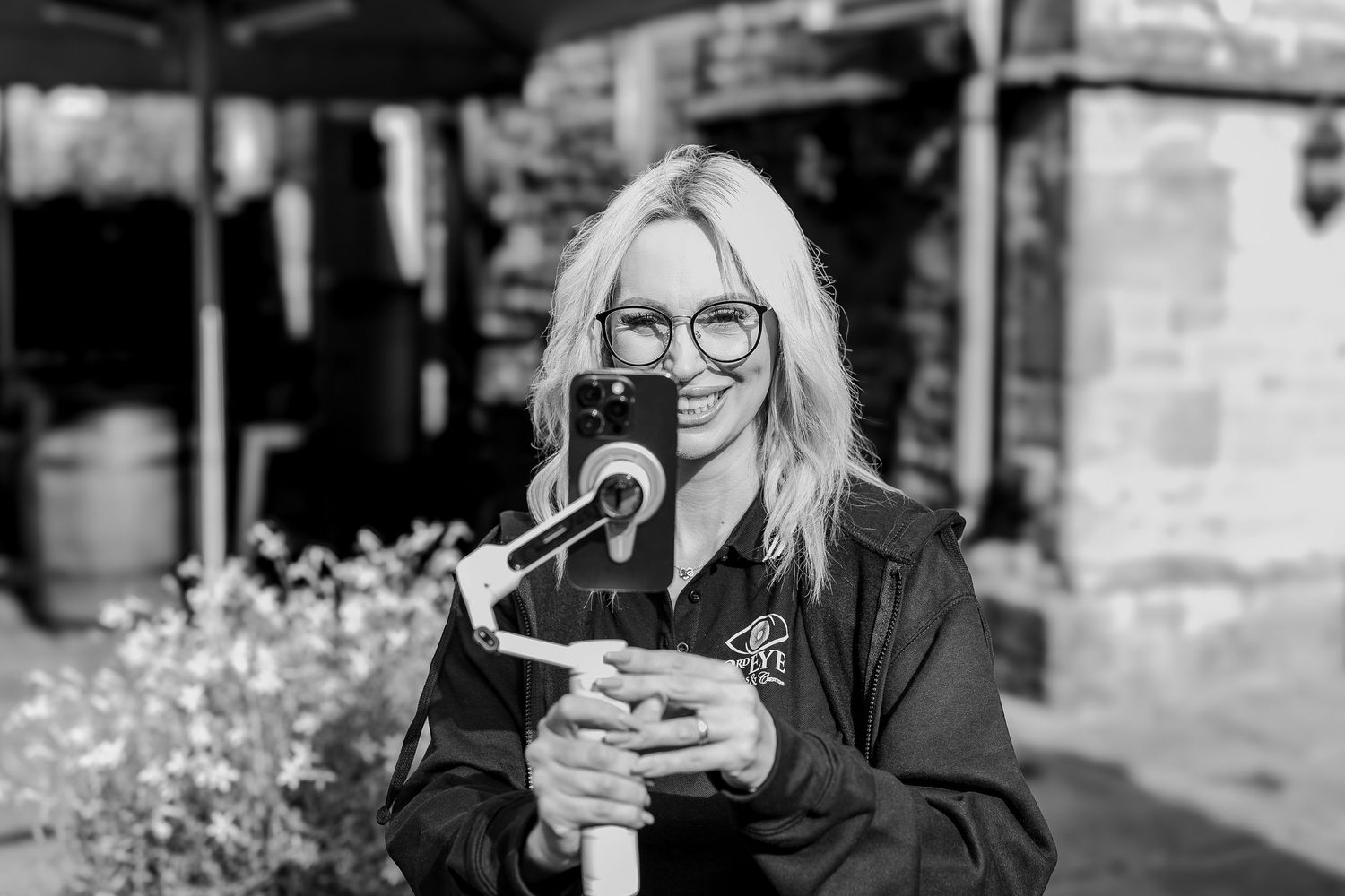 Content creator smiling outdoors on a sunny day, whilst filming a wedding.