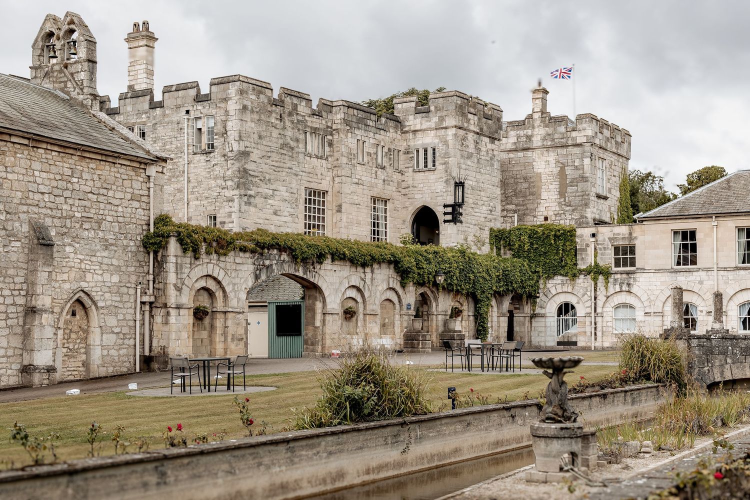 Historic stone castle facade with gothic arches and climbing vines under cloudy skies at Hazlewood Castle in Yorkshire.