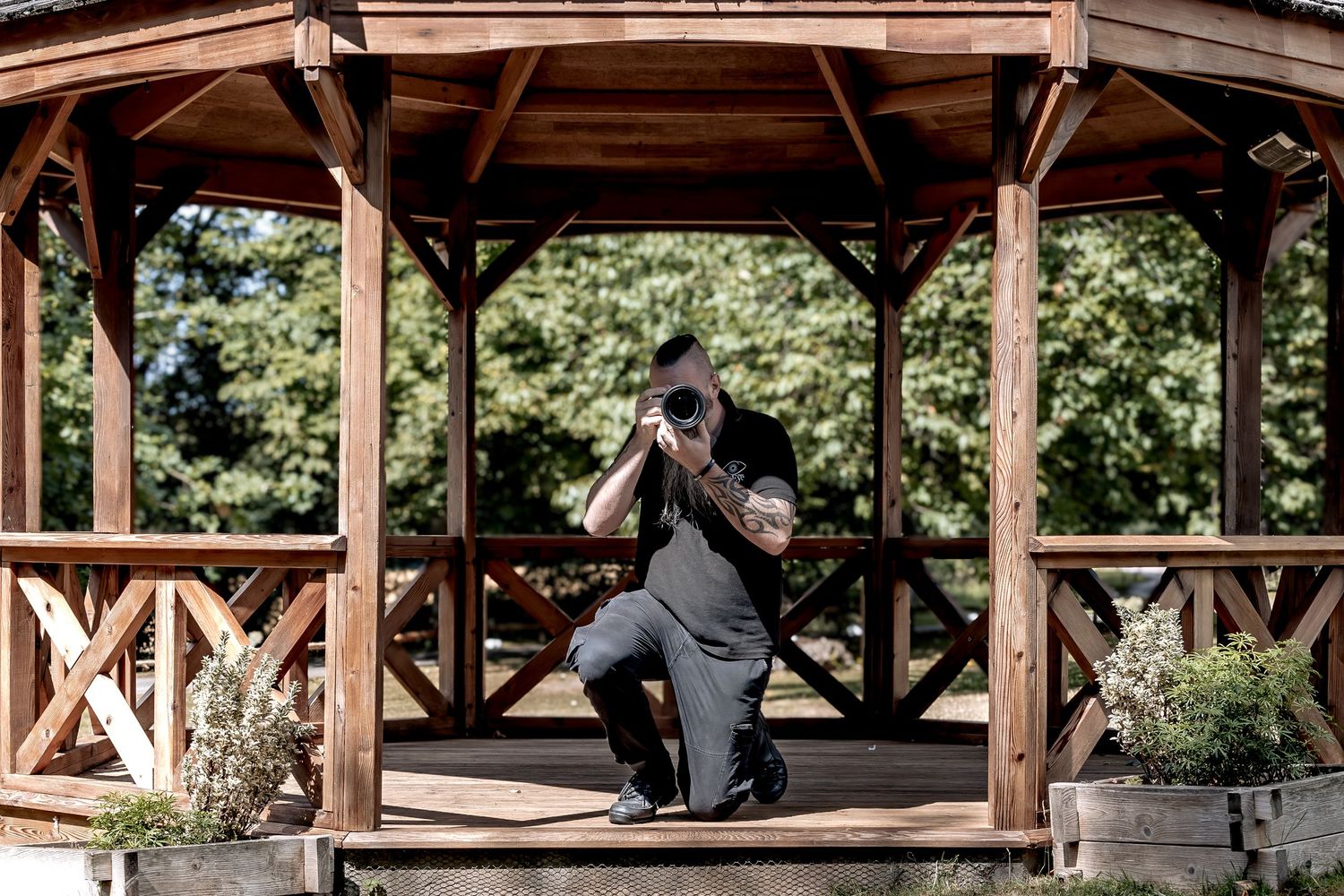 A rphotographer in rustic wooden pavilion with benches provides shelter in a serene park