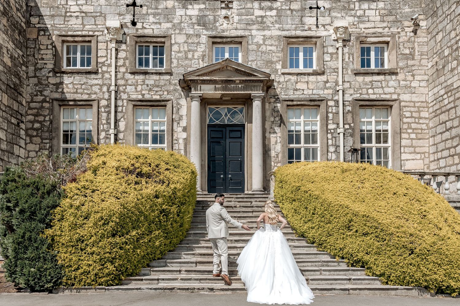 A bride led up the steps of Hazlewood castle by her groom on their wedding day.