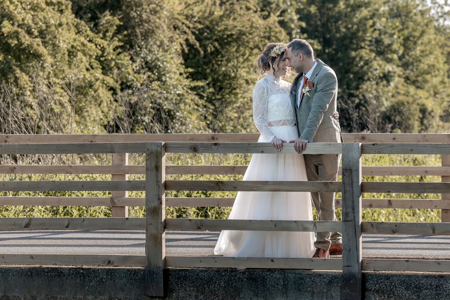 A couple in wedding attire shares romantic moments on a wooden bridge surrounded by lush greenery.