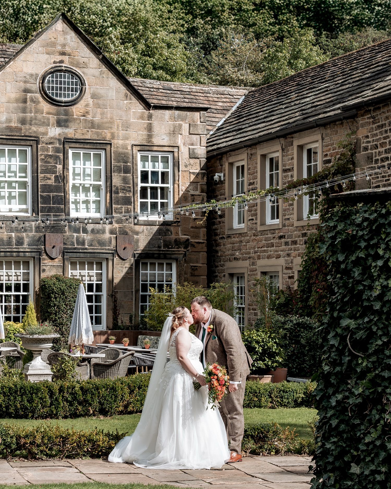A couple shares an intimate moment in front of a historic stone building with ivy-covered walls and traditional windows.