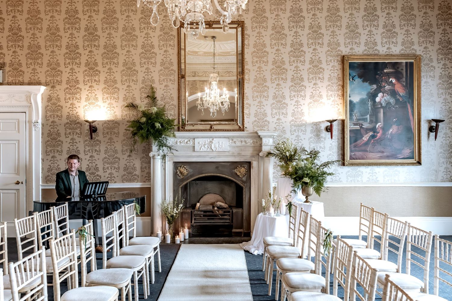 A panoramic view of an elegant wedding venue with white chairs, chandeliers, and ornate wallpaper in a traditional setting.
