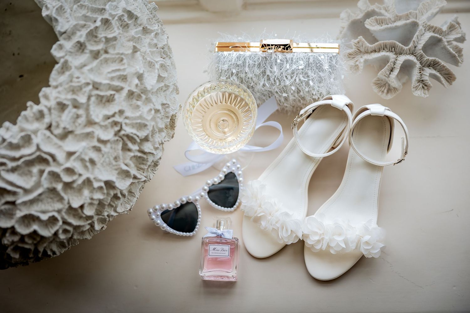 White paper tissue pom poms and elegant bridal accessories including shoes and perfume arranged for wedding photography.
