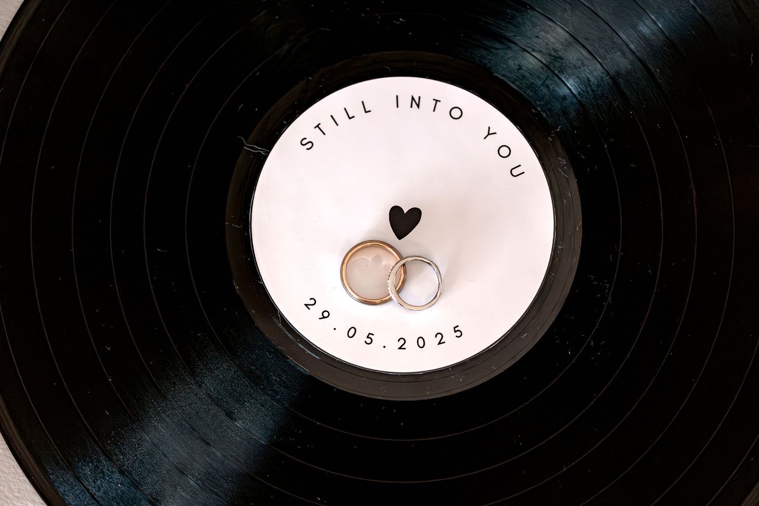 A close-up view of black vinyl record with wedding rings on top.