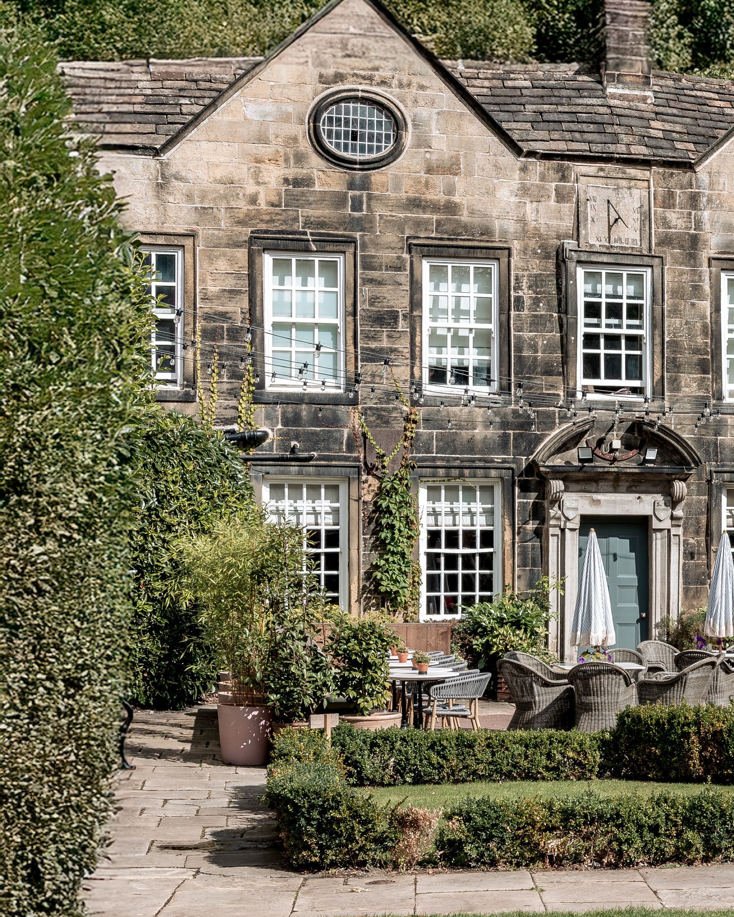 Historic stone building with traditional windows and architectural details surrounded by green shrubbery and trees.
