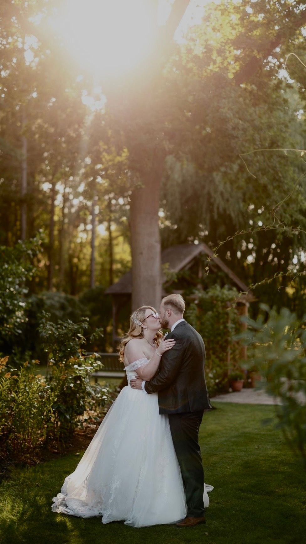 A romantic sunset wedding photo in a lush garden with golden sunlight streaming through the trees.