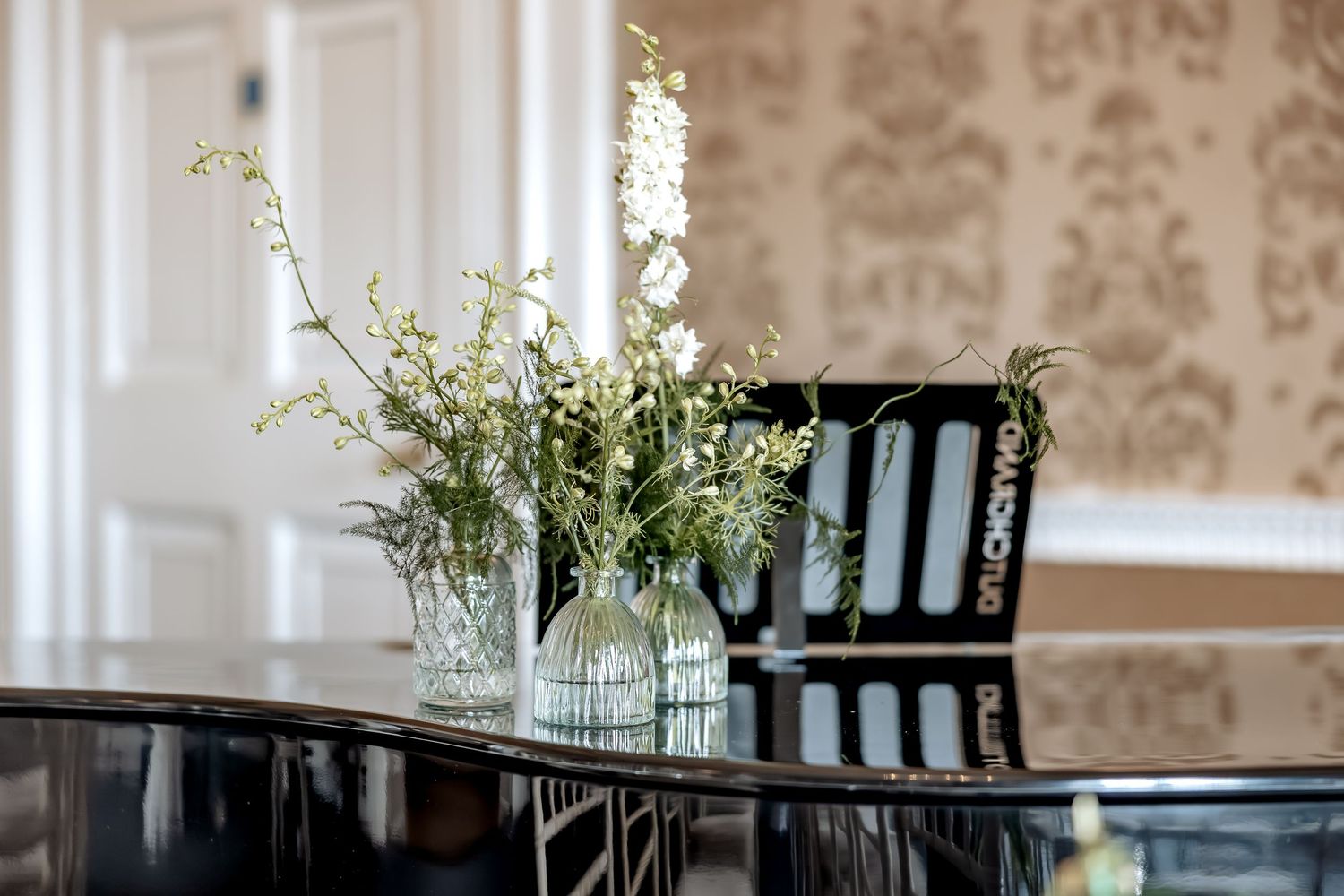 An elegant dining room features damask wallpaper, dark wood furnishings, and white floral centerpieces on piano.