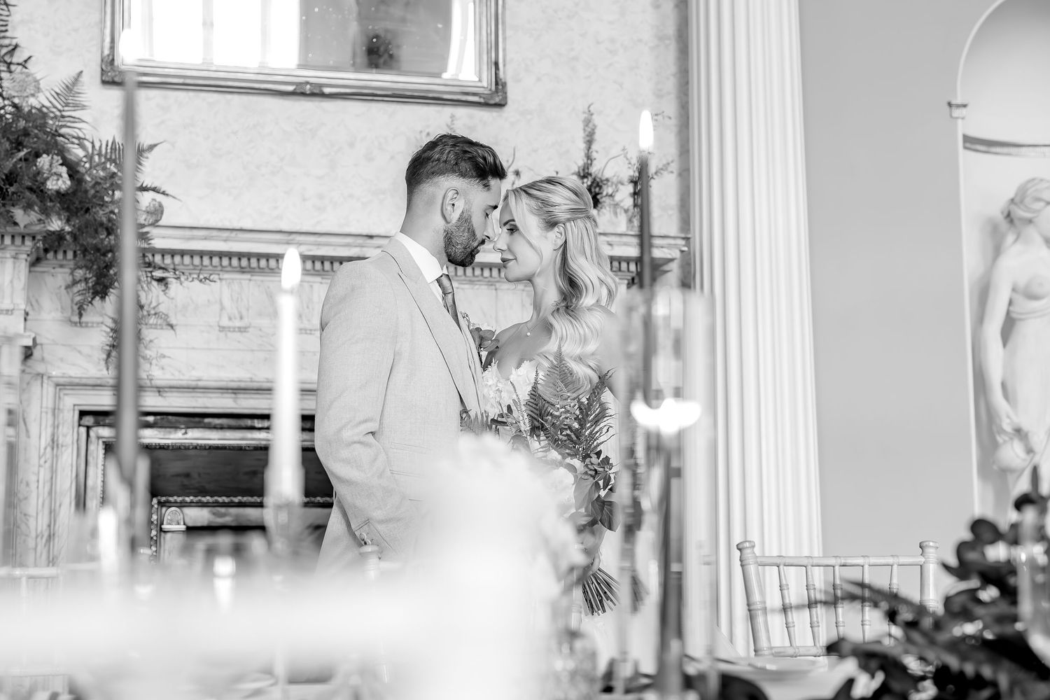 A romantic black and white wedding photo of a tender moment between two people in an elegant indoor setting.