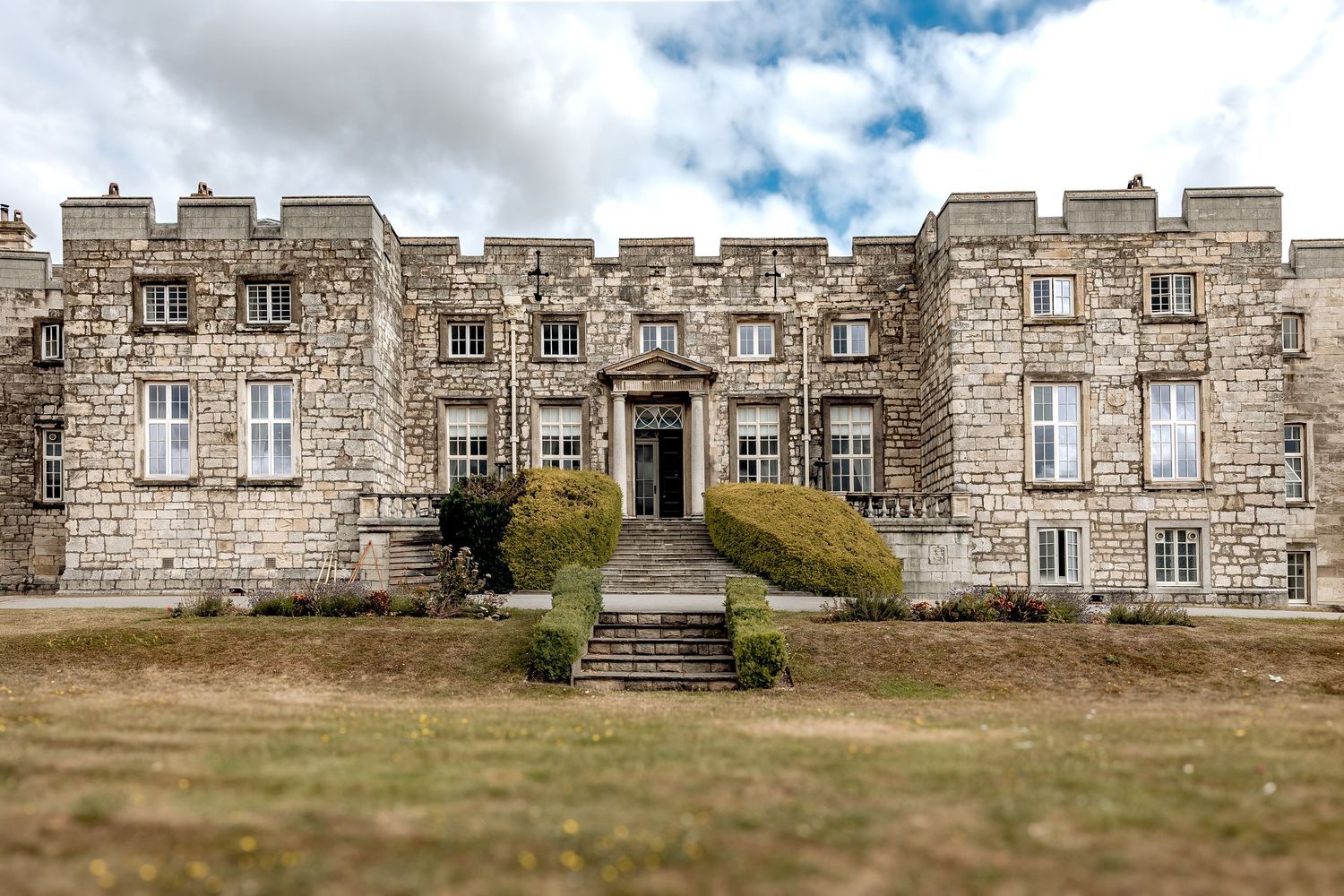 Historic stone castle building with symmetrical facade and central entrance stairs under cloudy skies in Yorkshire.