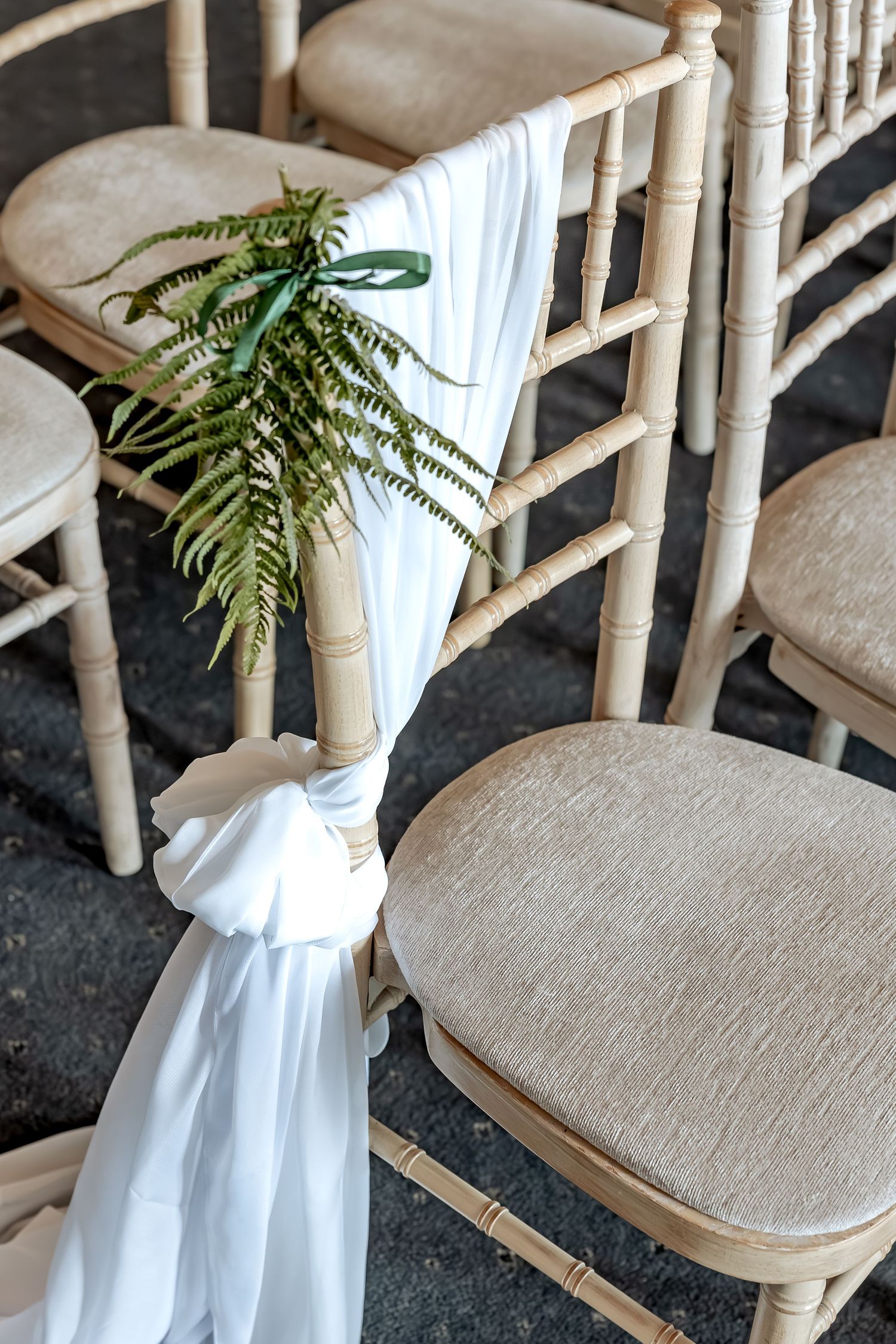 White fabric draping and fern leaf decorate a rustic bamboo chair at wedding ceremony seating arrangement.