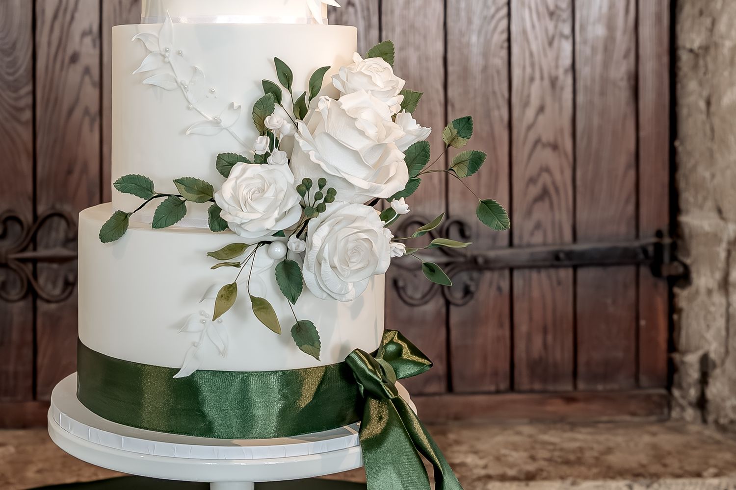 Elegant white wedding cake decorated with fresh roses and eucalyptus leaves against rustic wooden backdrop.