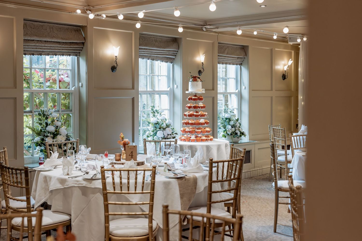 An elegant white wedding reception venue with chiavari chairs and round tables set for dining under soft lighting.