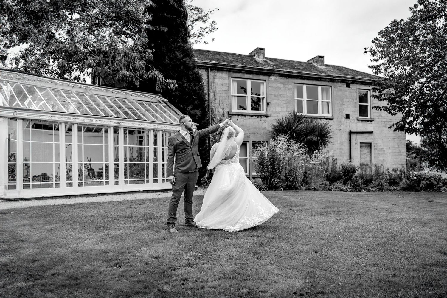 A bride and groom dance together on a grassy lawn outside a stately building during their wedding celebration.
