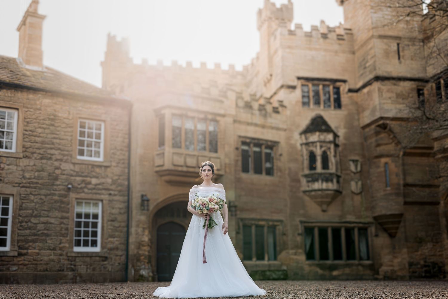 A bride in a white wedding gown poses in front of a historic stone building during a golden sunset.