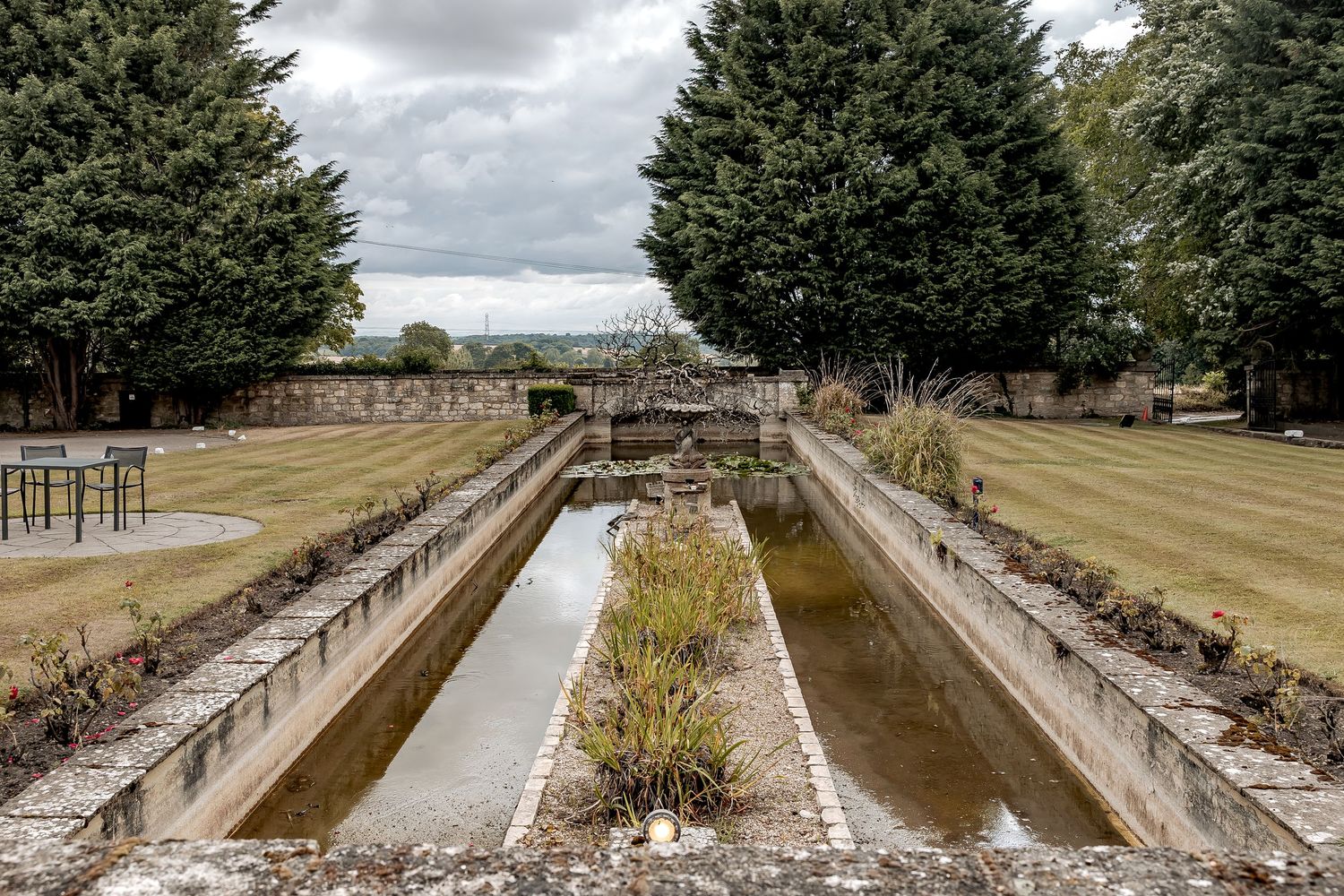 Historic castle pond with parallel stone walls and water channels viewed from above on a cloudy day.