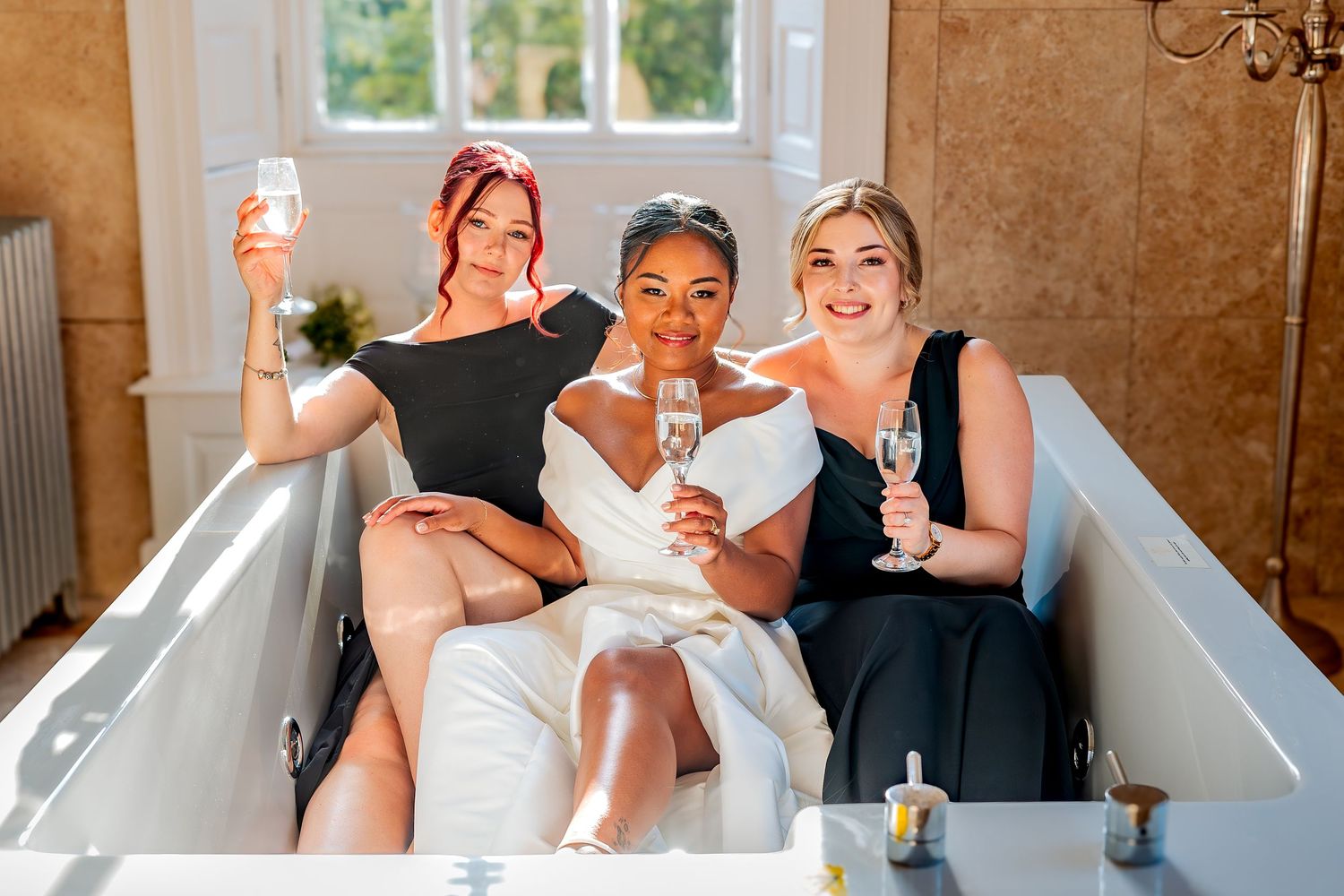 A bridal party holding champagne glasses together in an elegant bathroom with neutral decor for a wedding toast.