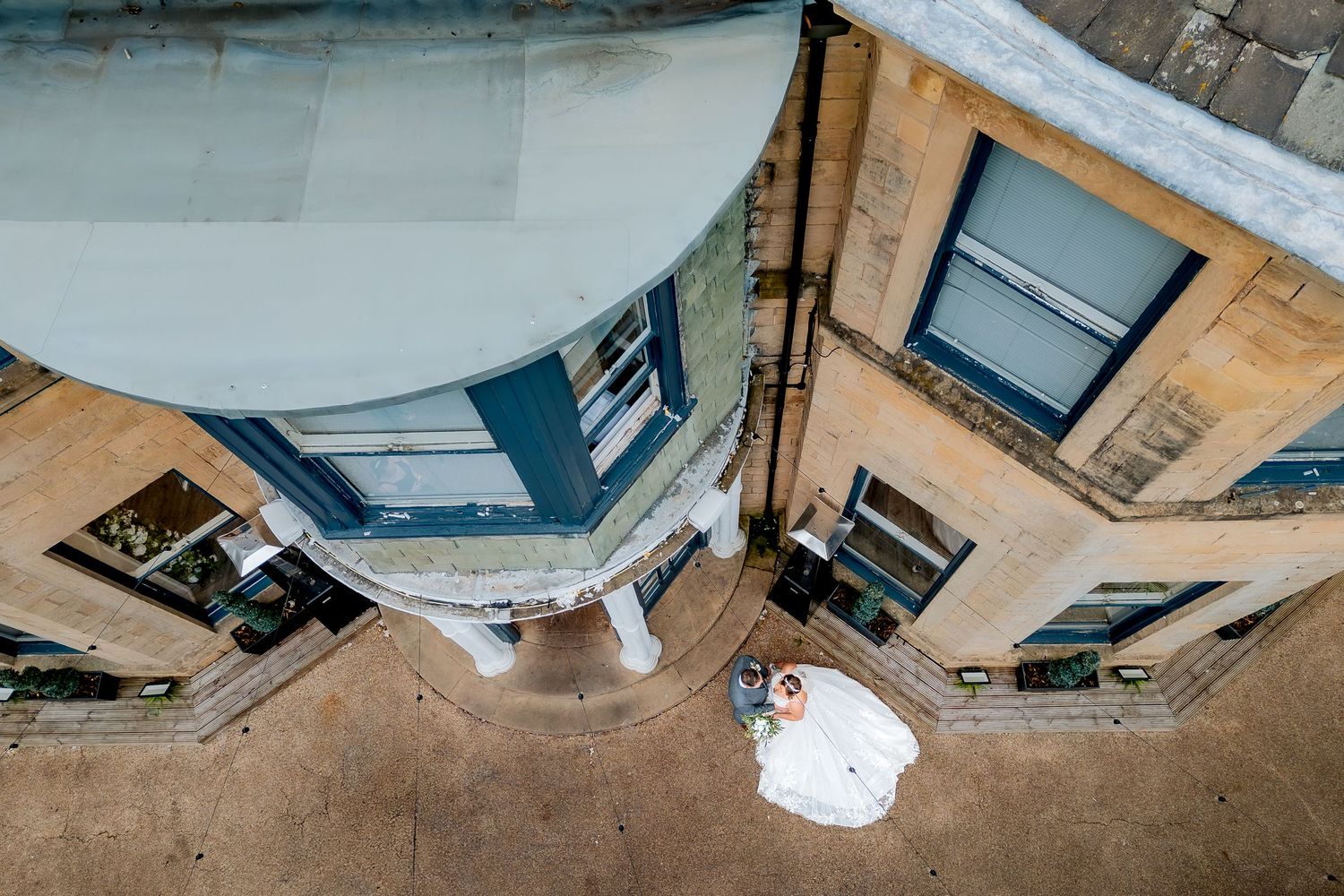 A drone shot from above a tall wedding venue shows off the venue and newly weds.